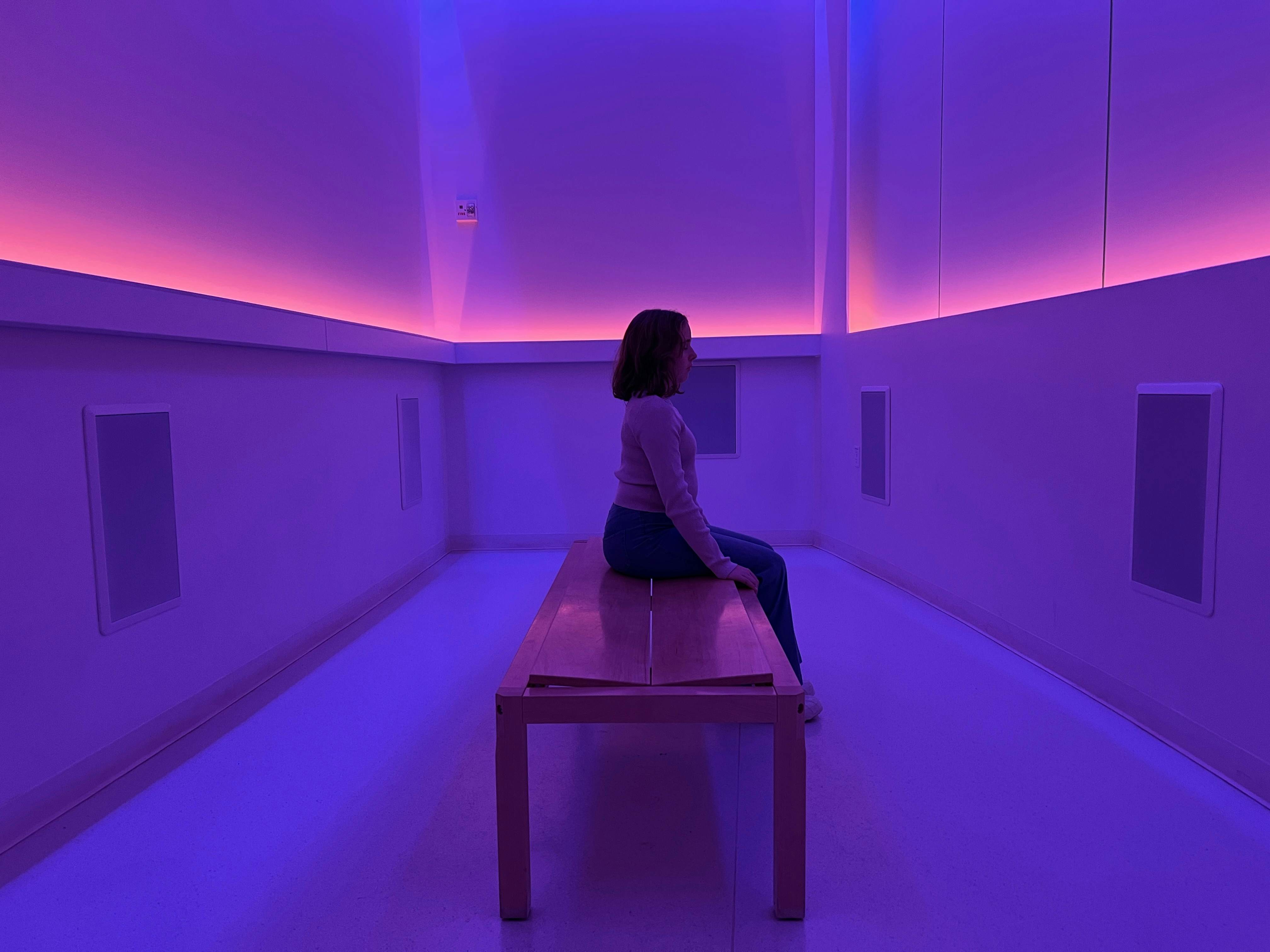 A person sitting on a bench in a room filled with purple and magenta light.