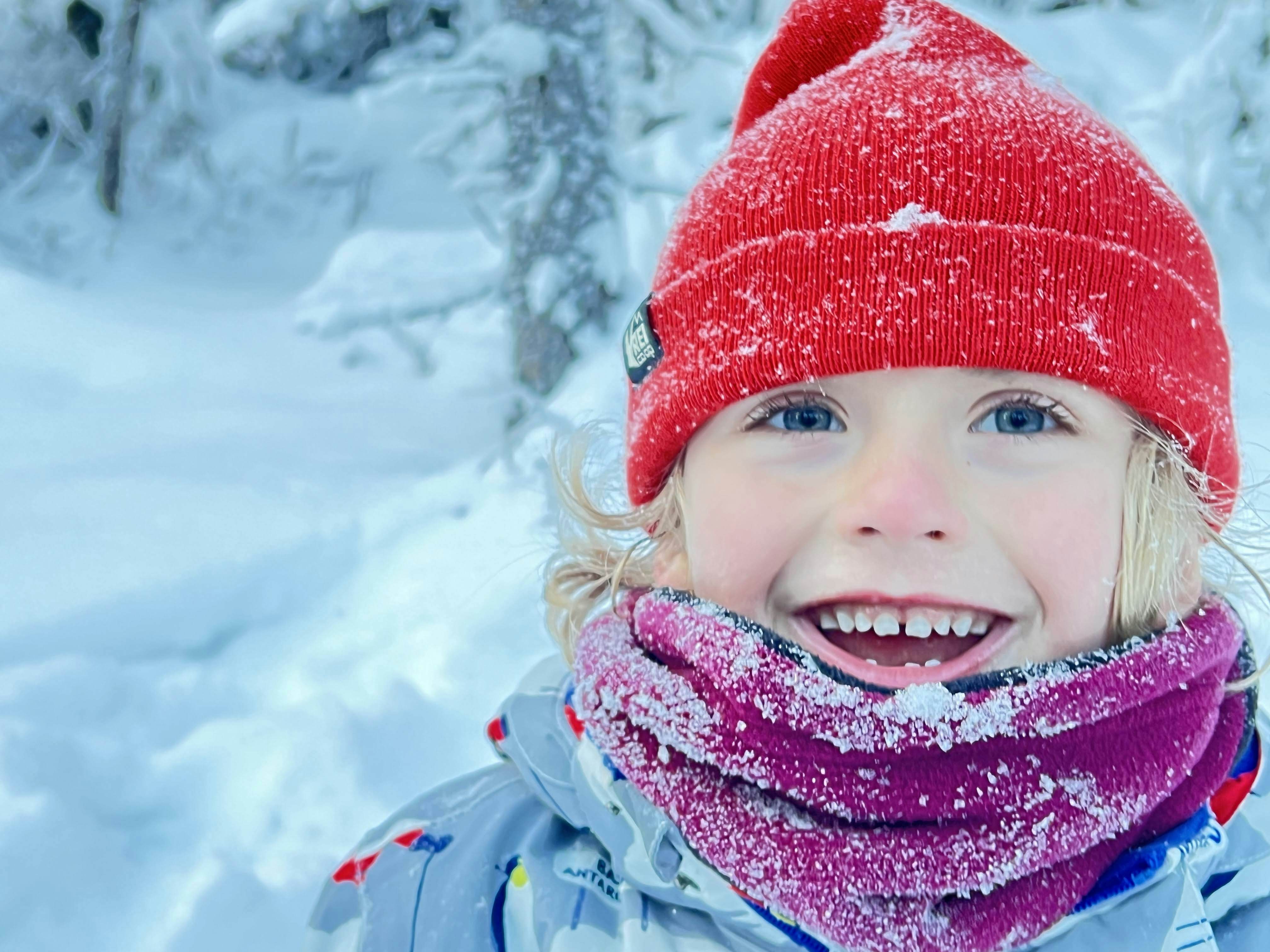 A boy wearing a red hat smiles in a snowy landscape in Fairbanks, Alaska.