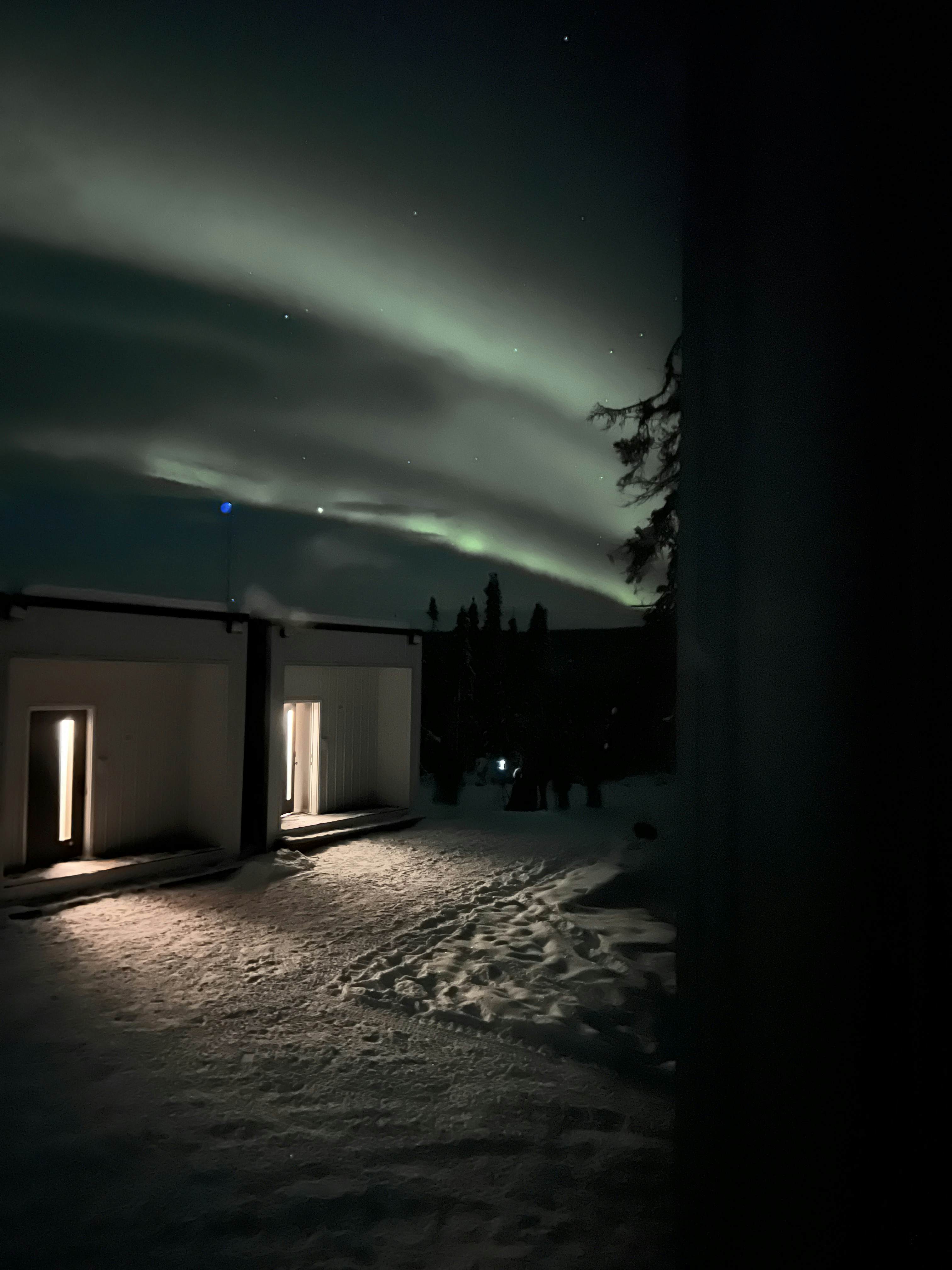Streaks of northern lights over a squat square building in the snow in Alaska.