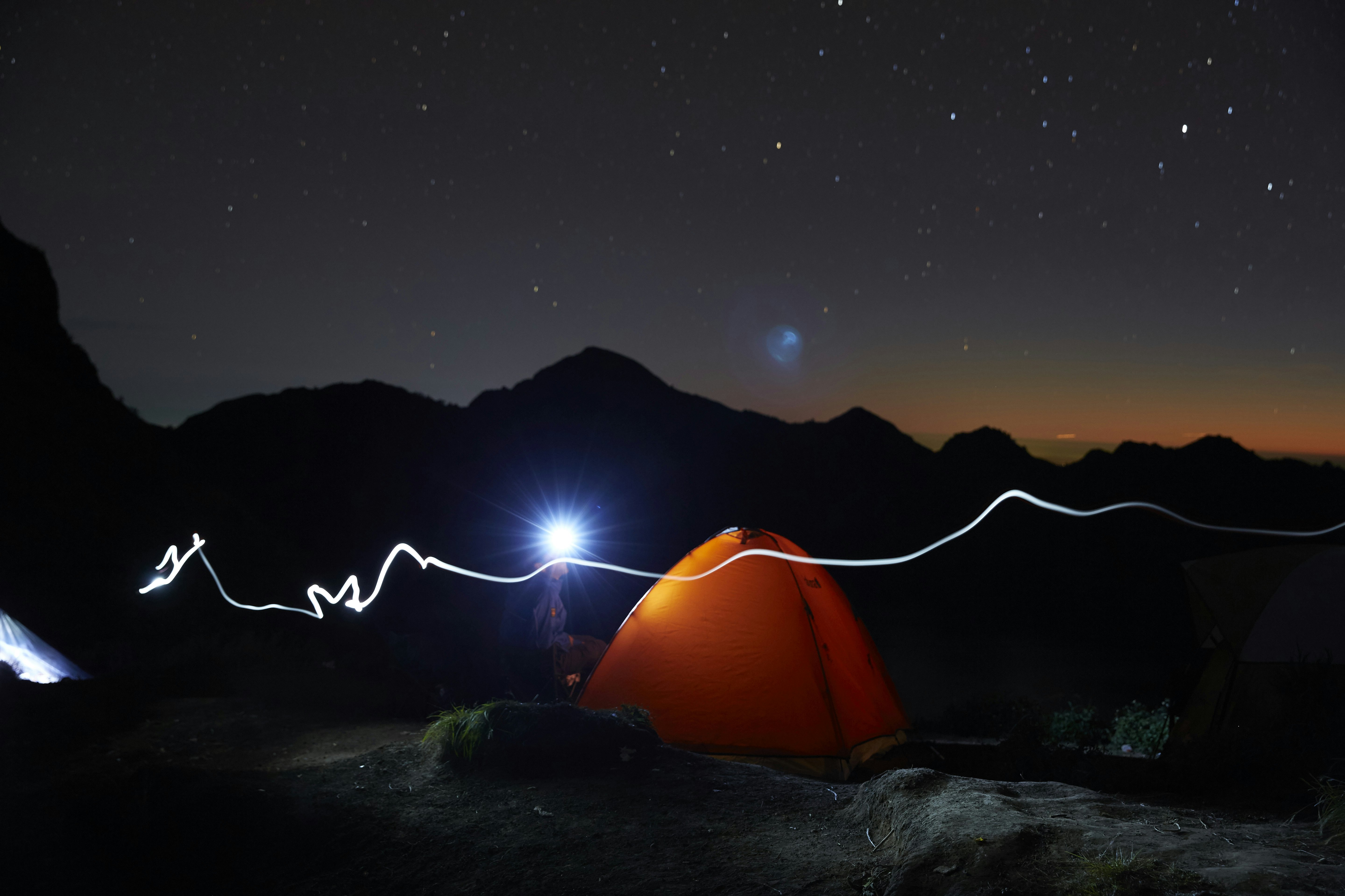 An orange tent shines brightly in the dark night with a mountain in the background