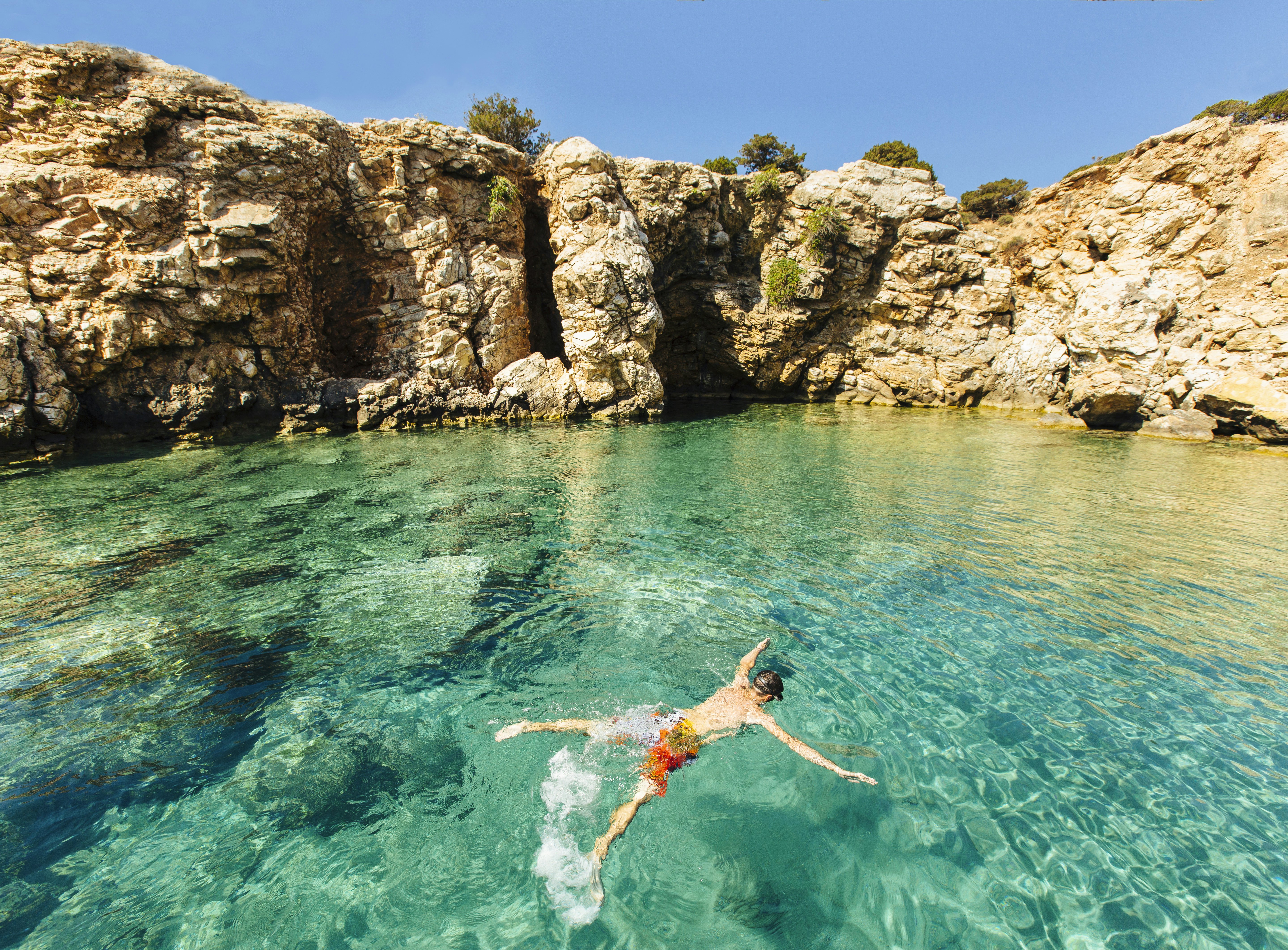 A person snorkels in turquoise water by boulders