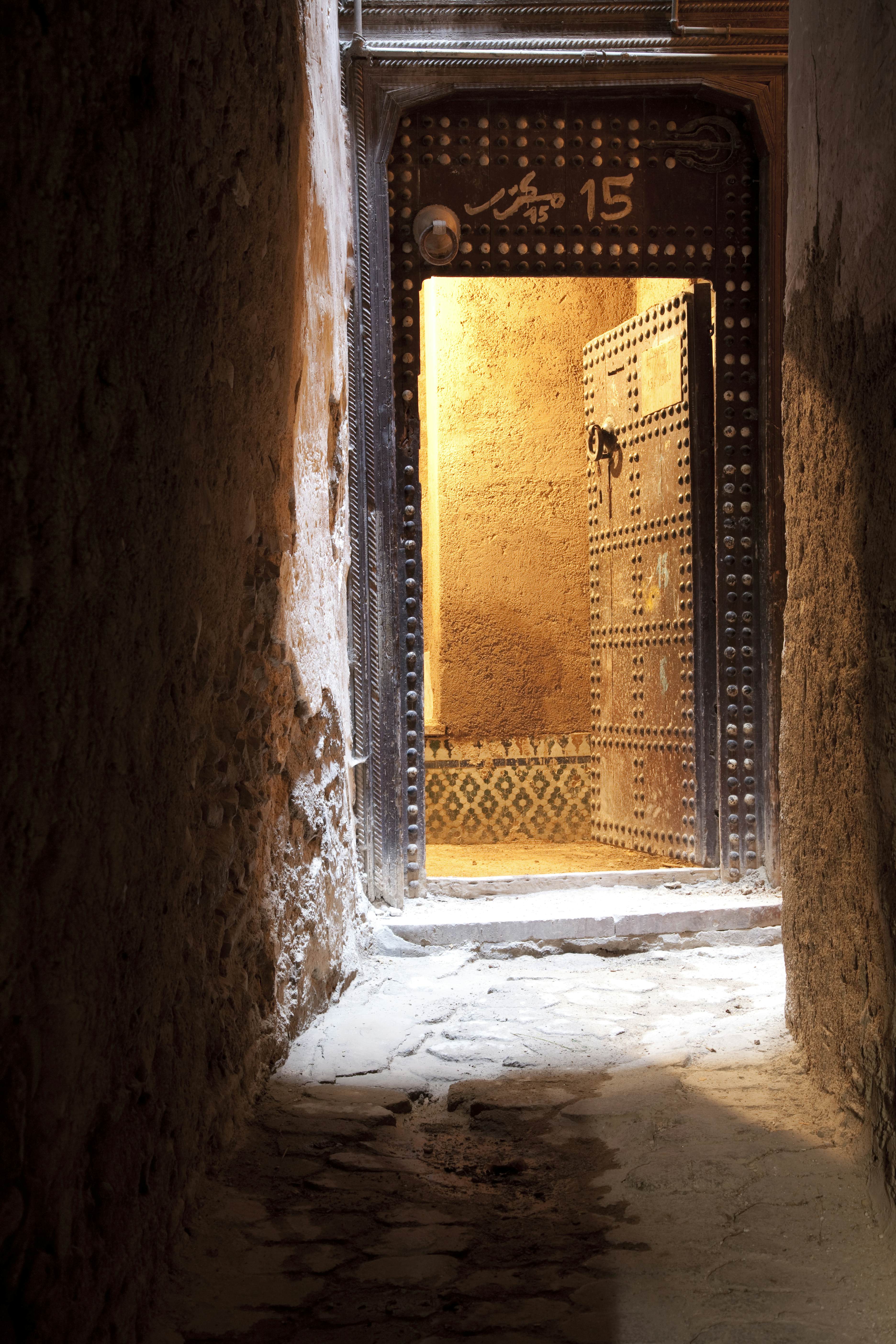 A shaded alley ends at a carved open doorway in Morocco.