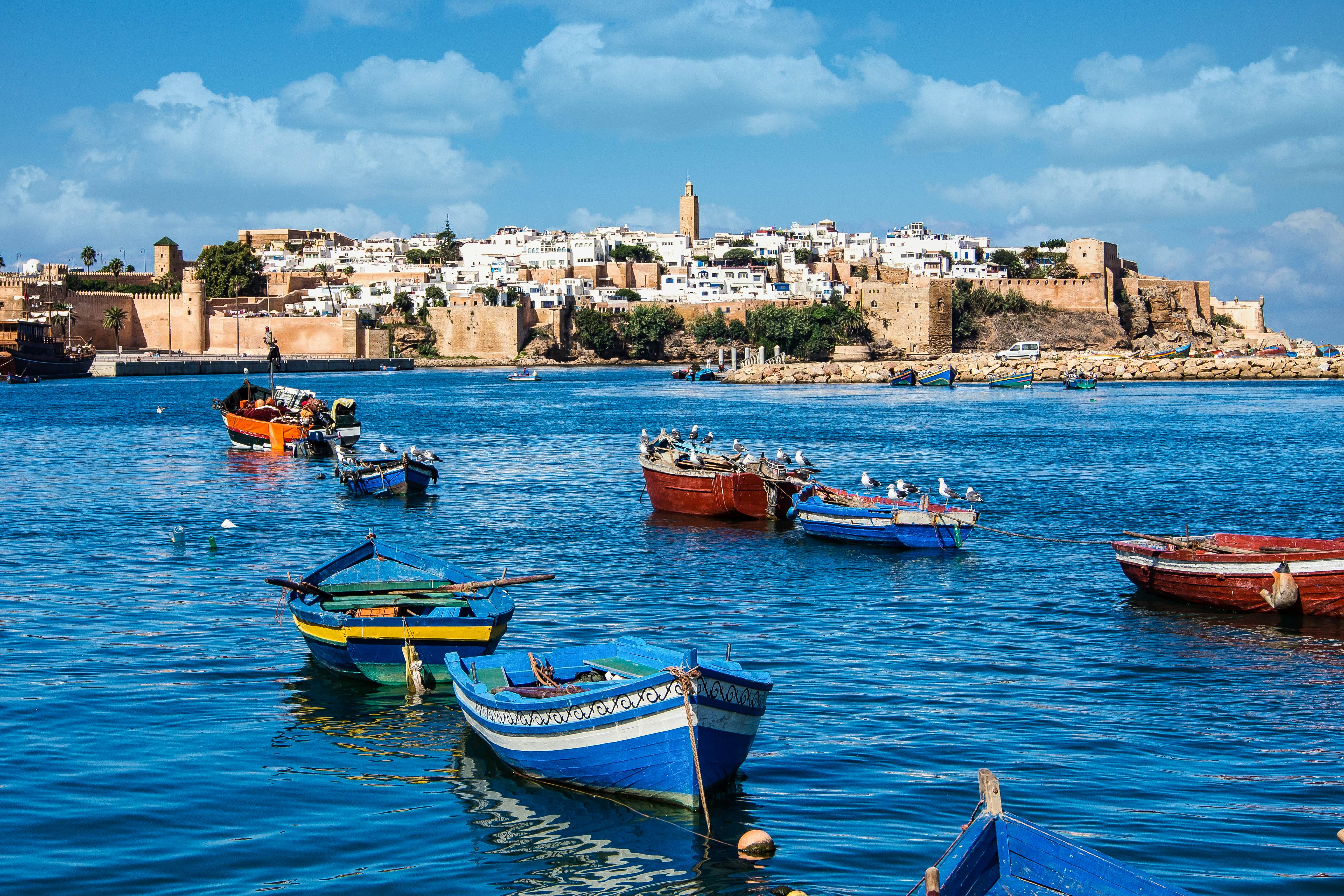 Boats in blue water; a fort is on the shore and a low-rise city behind it.