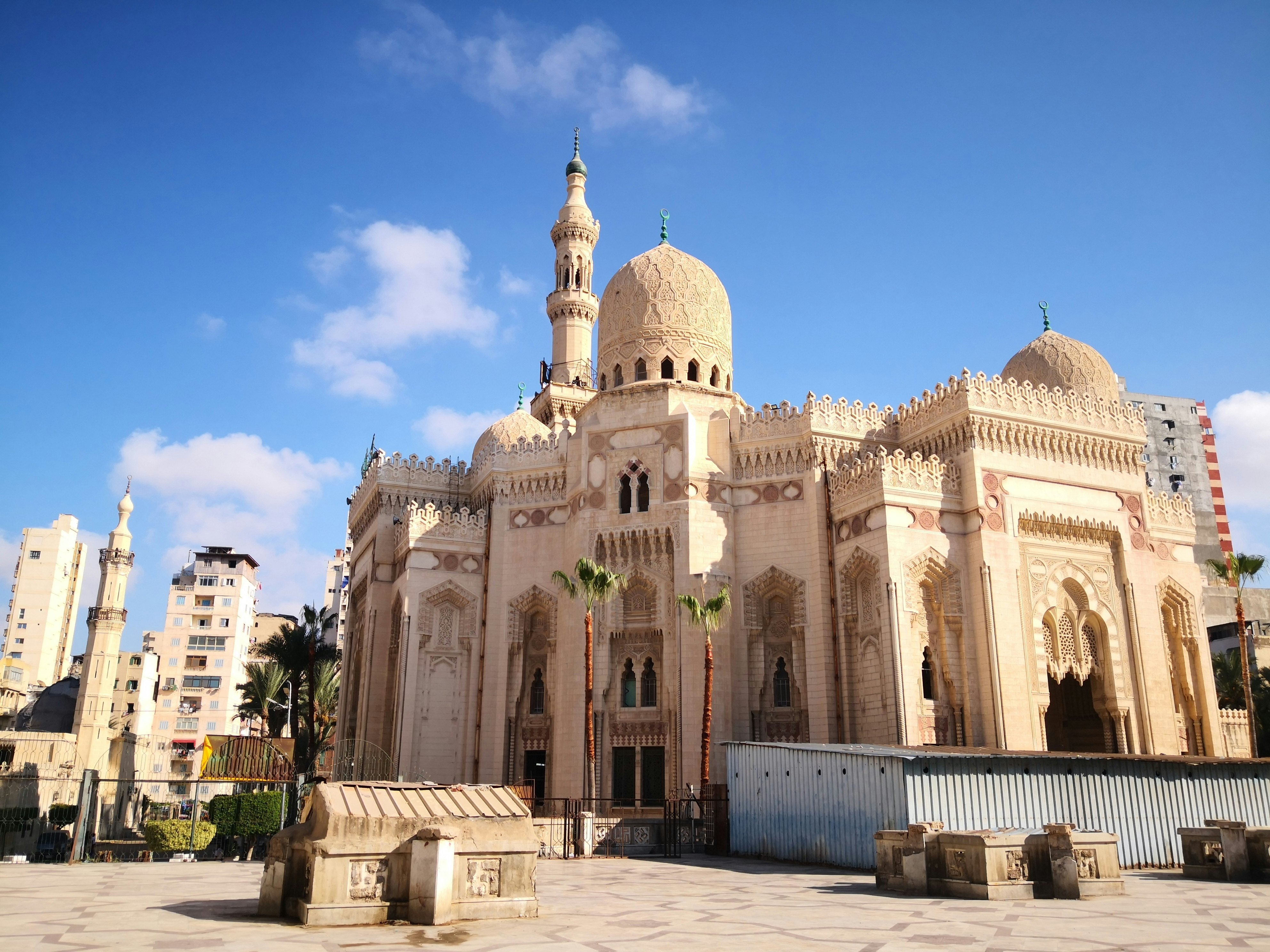 The tan domes and minaret of a mosque in Egypt, under blue sky.