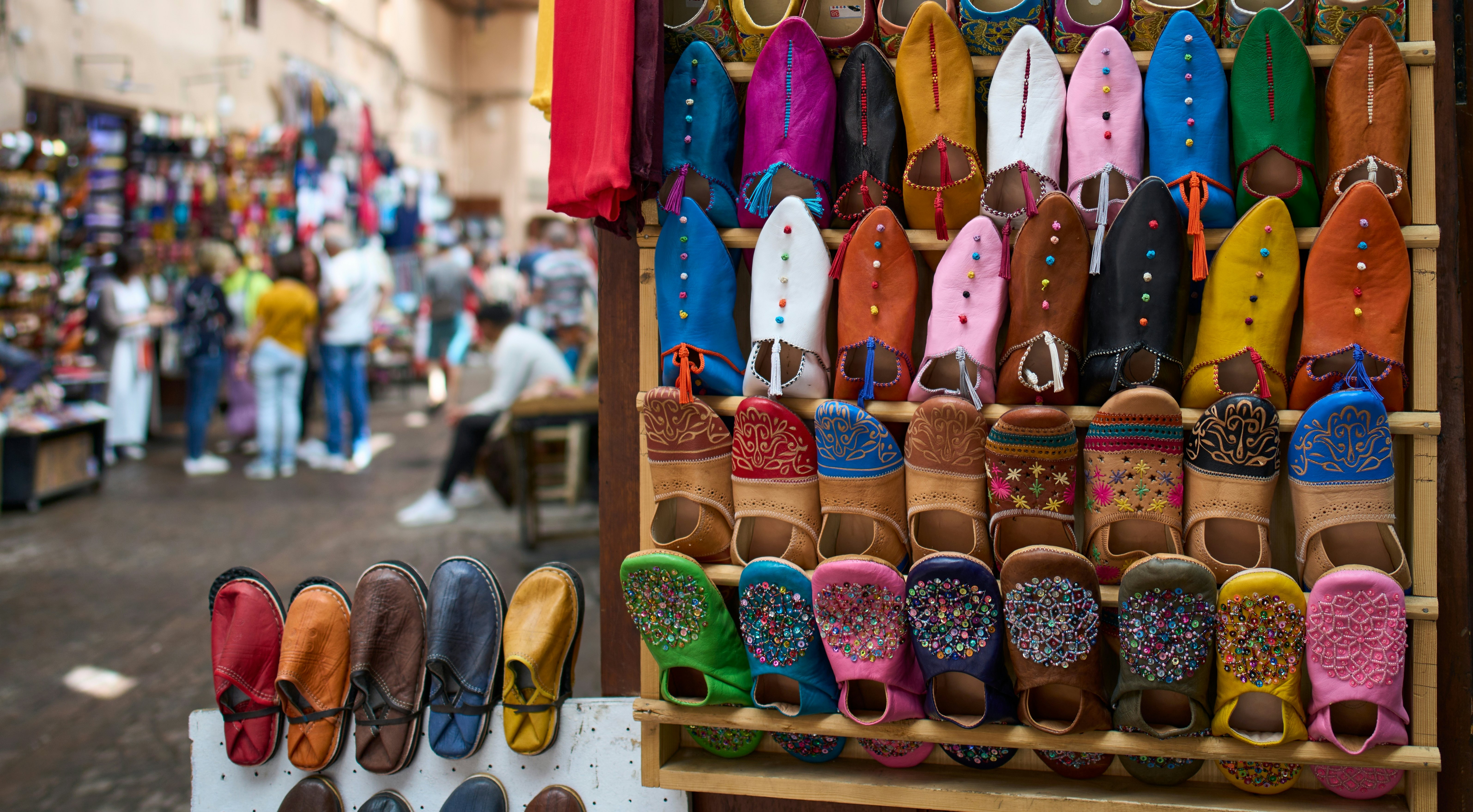 A series of brightly colored leather slippers in pairs on a wall rack.