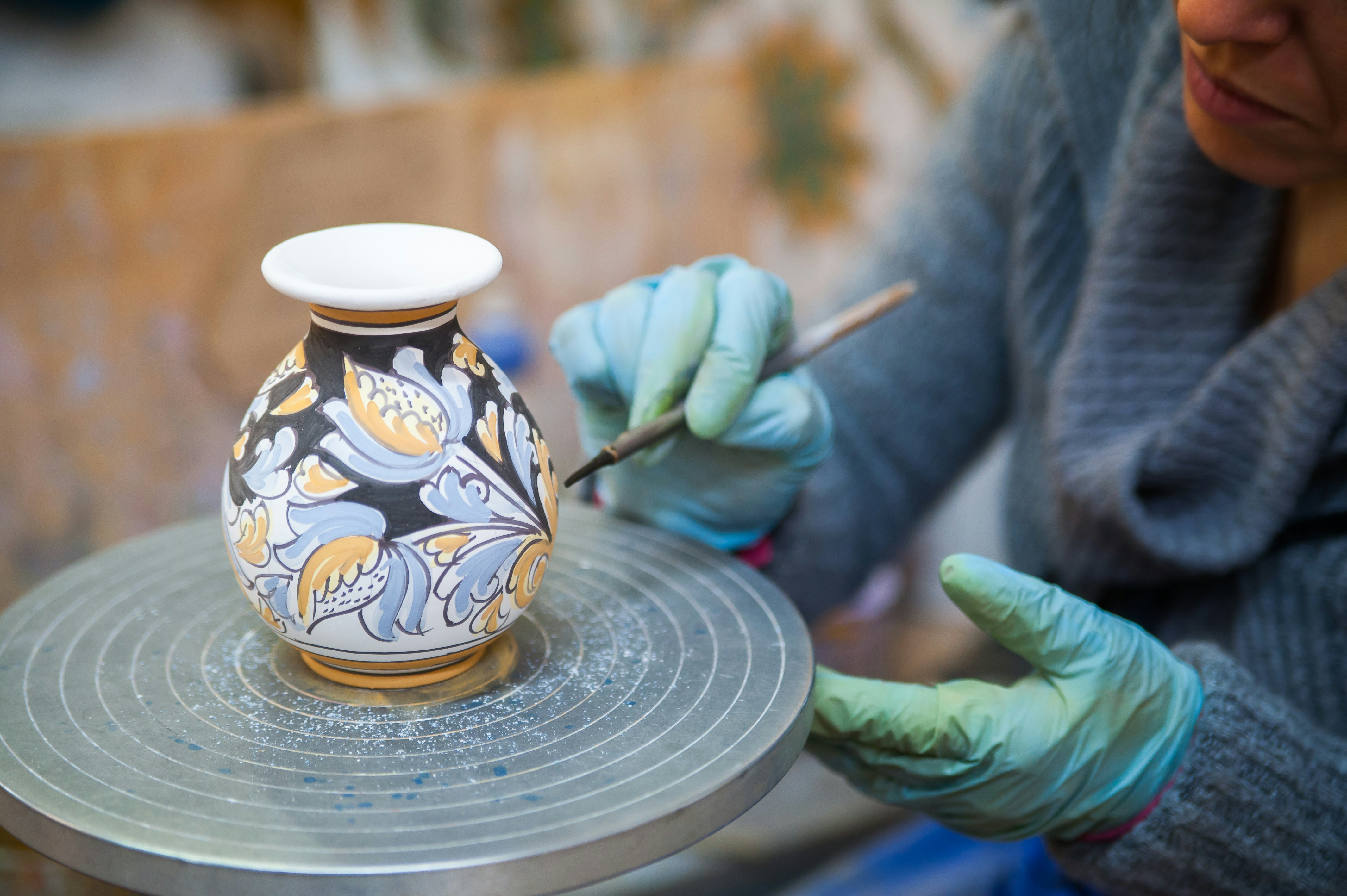View of a ceramic vase on a potter's wheel being decorated by a local artisan with a paintbrush.