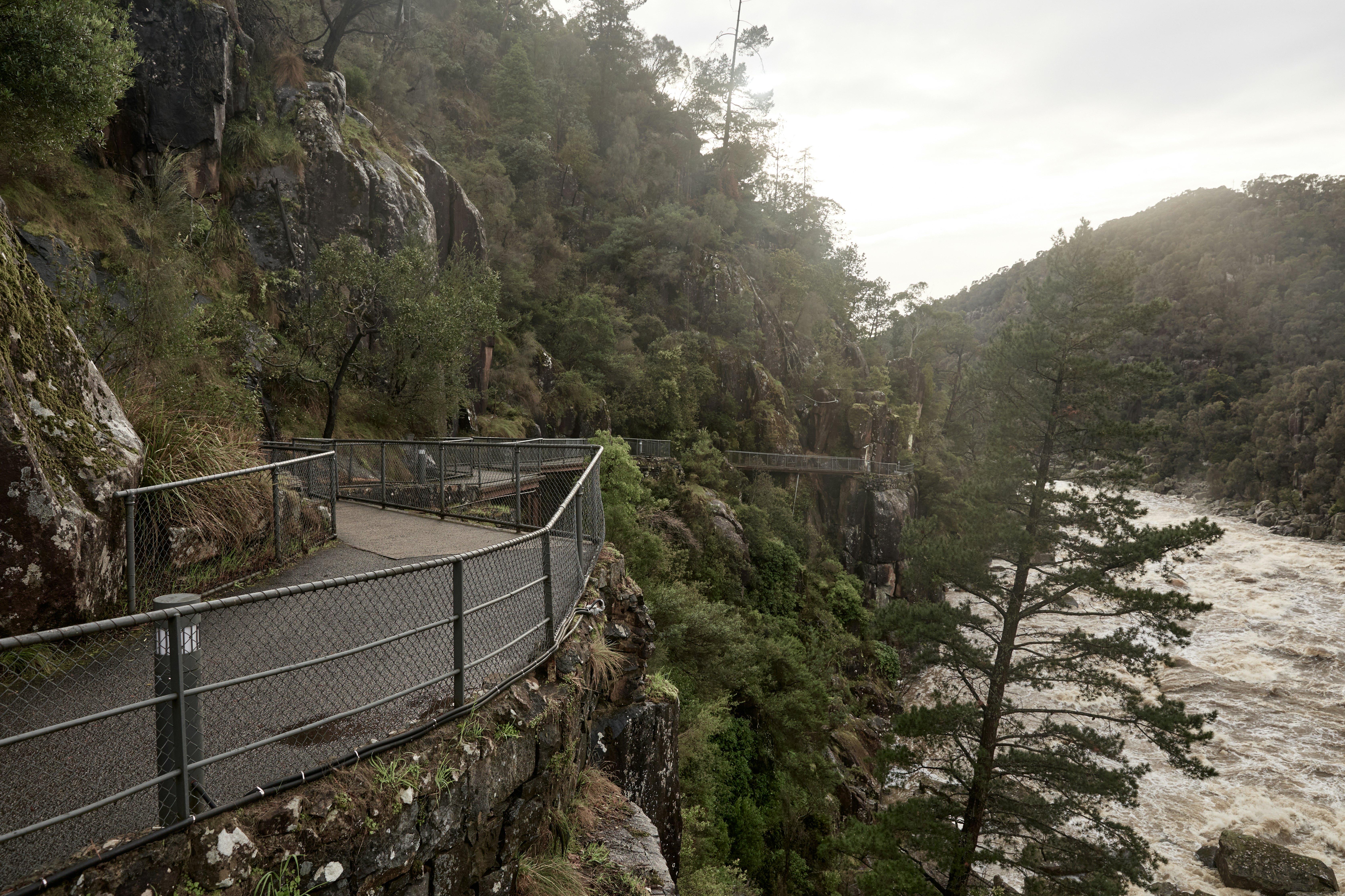 A black path next to a river and green hills