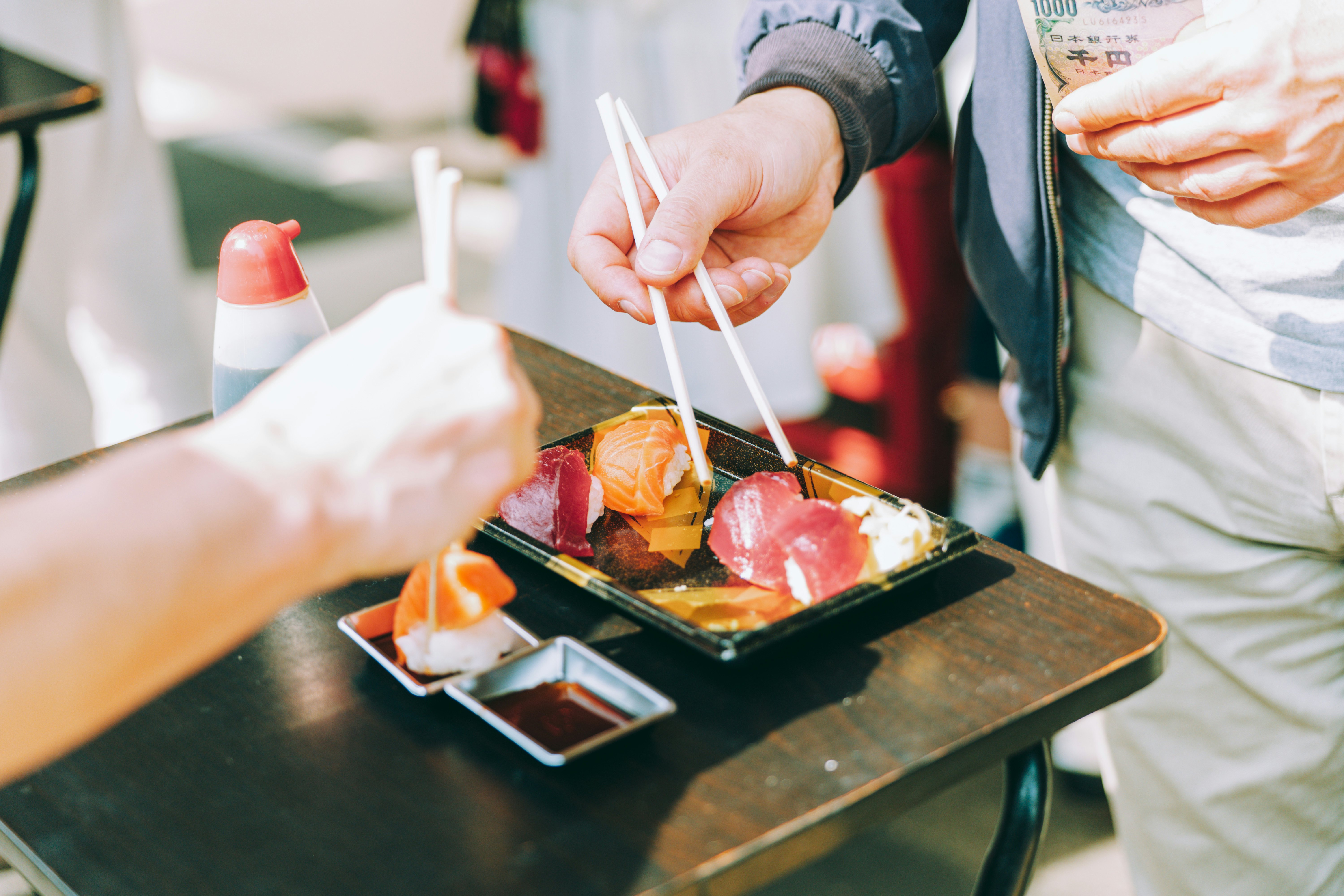 Two people sharing some sushi of salmon and tuna on white rice.