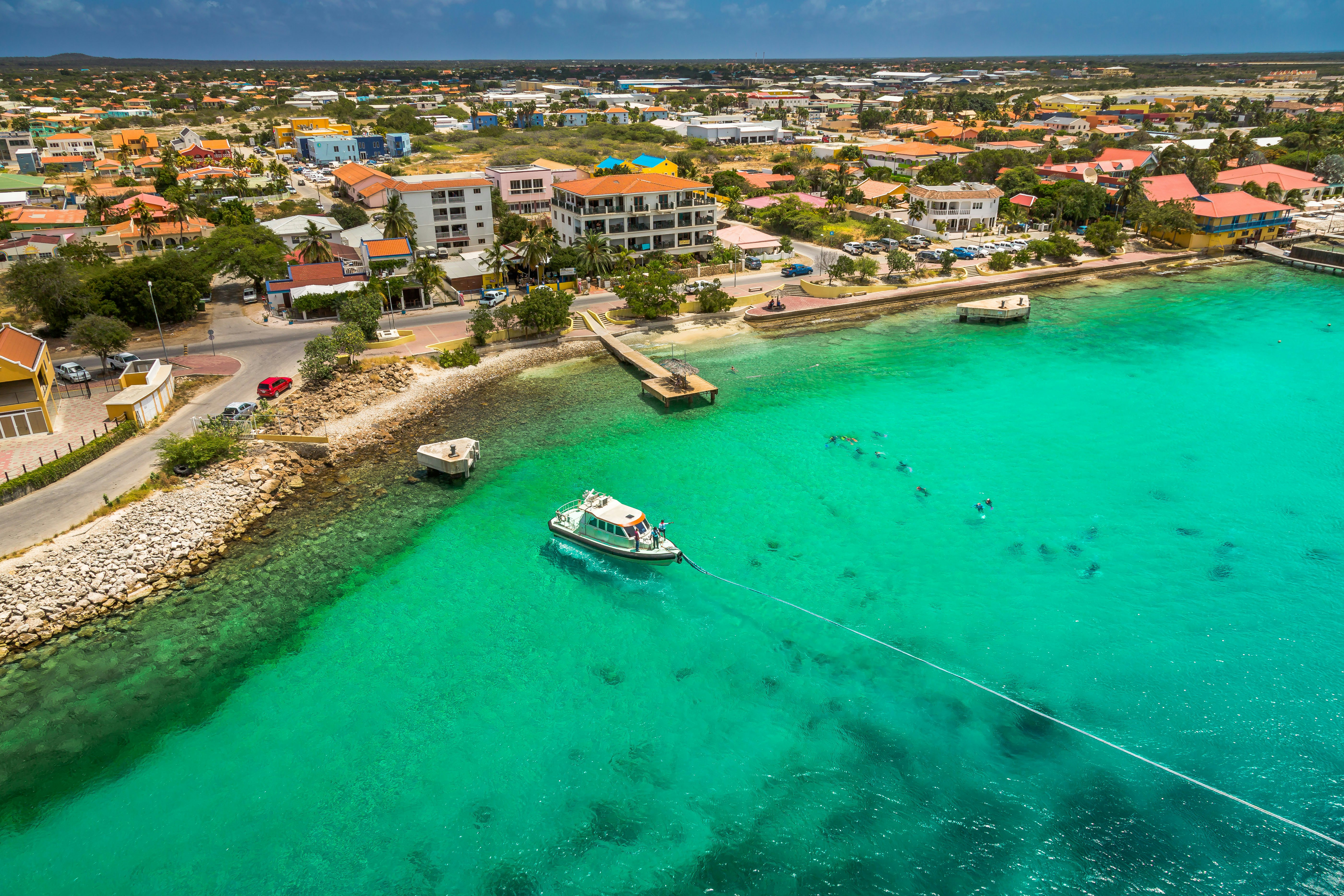 The waterfront of a small city in a tropical location. The shallow water is greenish blue, and a boat is in the port.