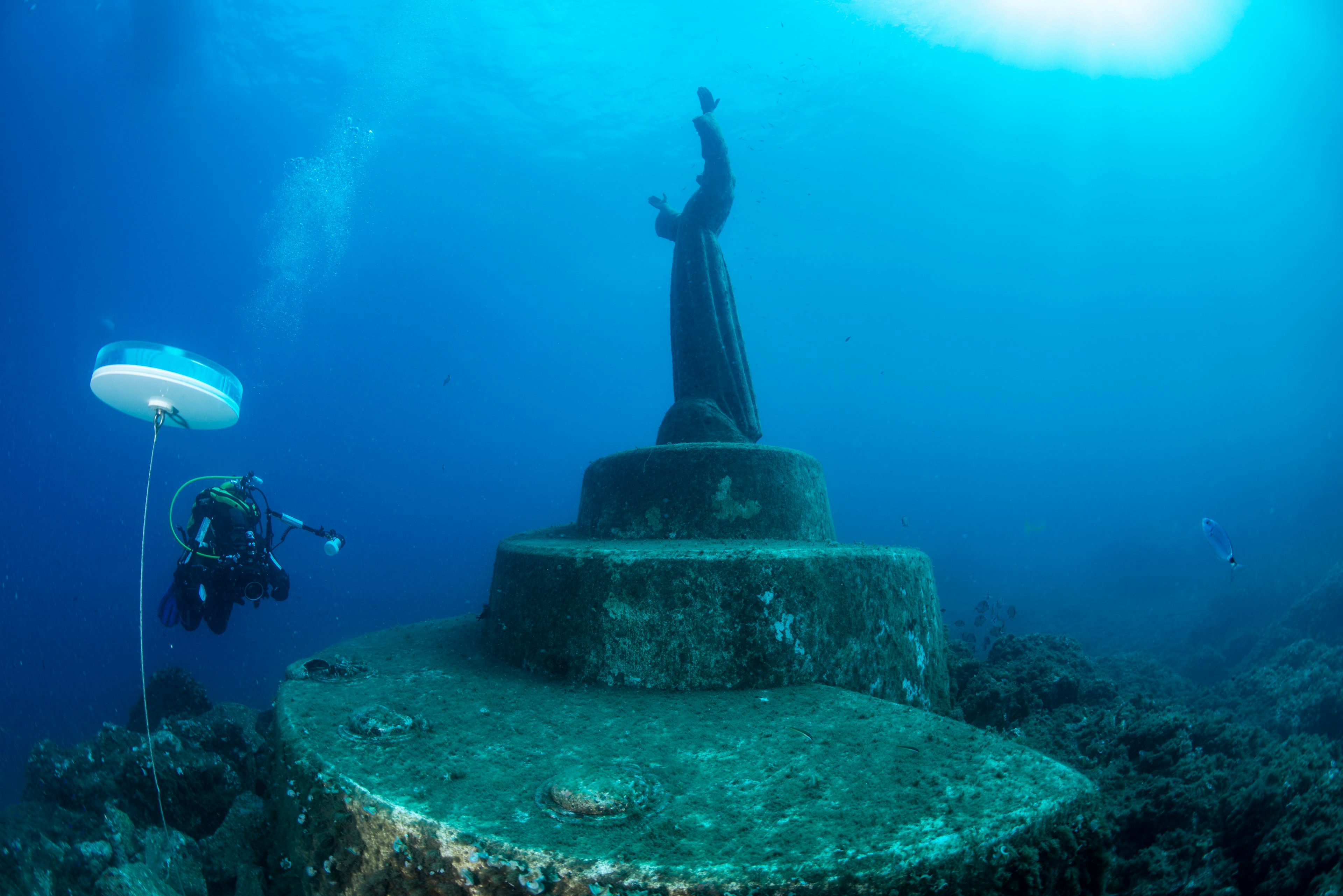 A diver swims near an underwater statue of Christ