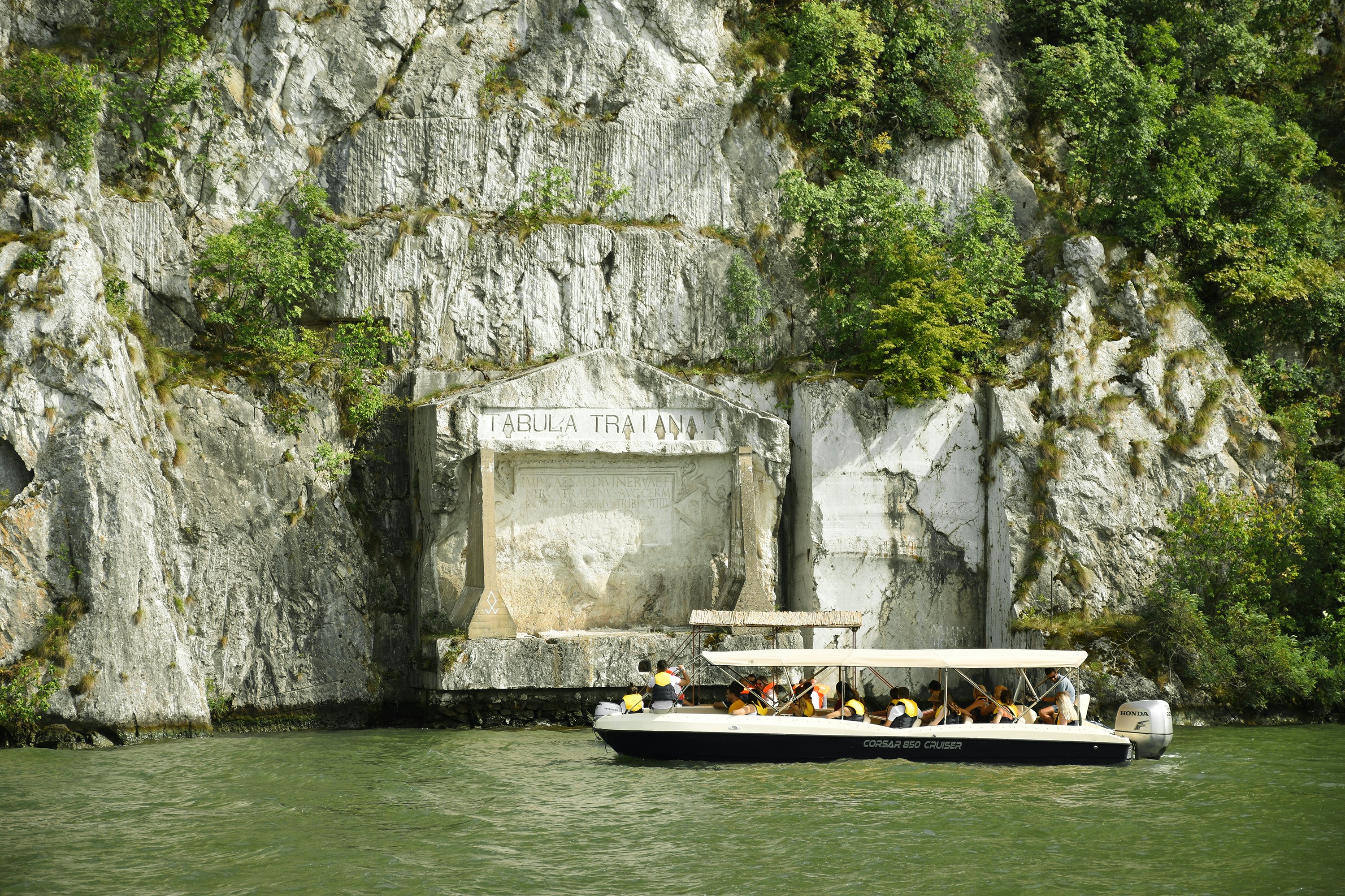 a sightseeing boat on a green river with huge rocks behind