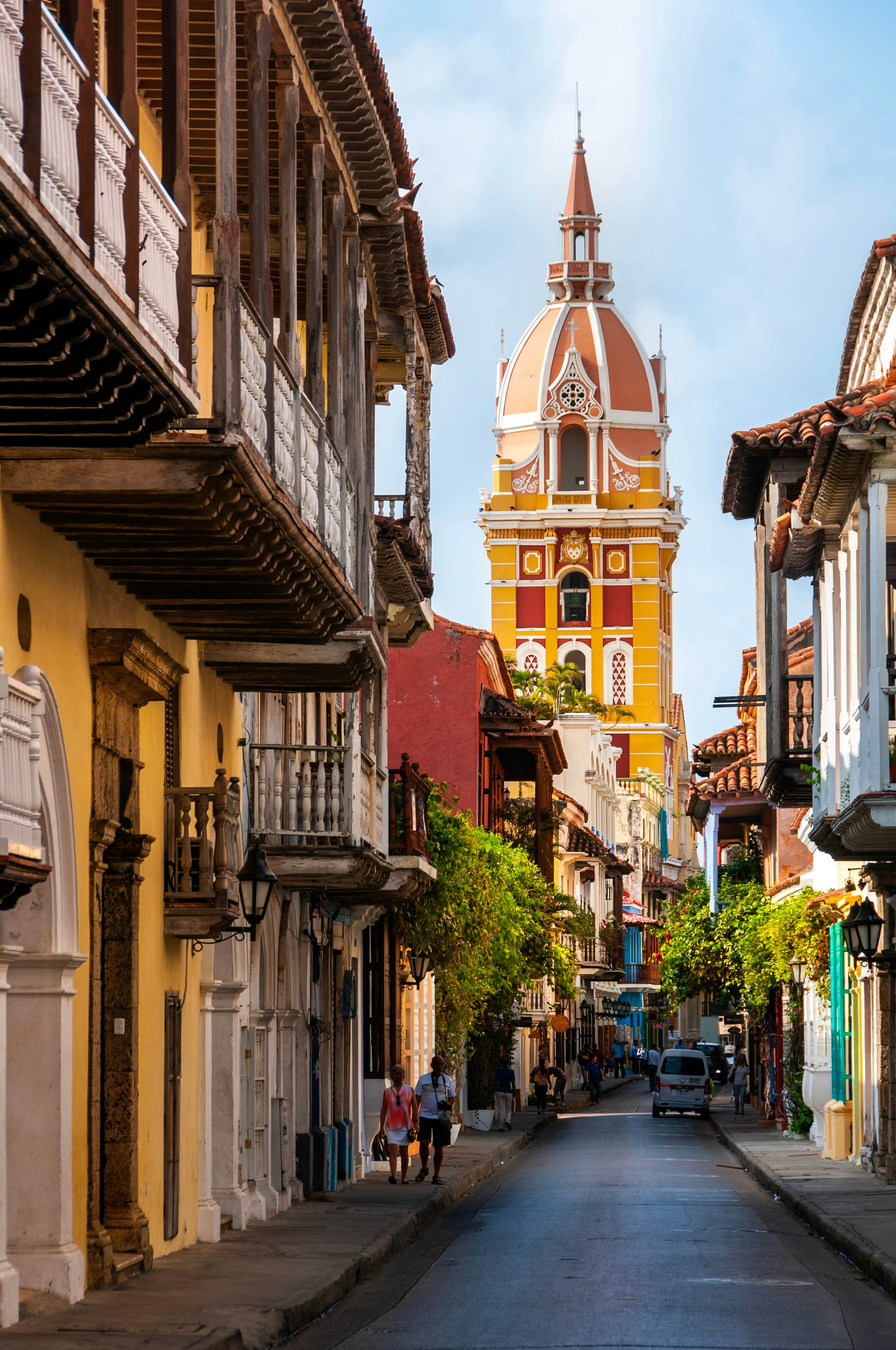 A yellow tower against blue sky at the end of a narrow street in a town's historic center.