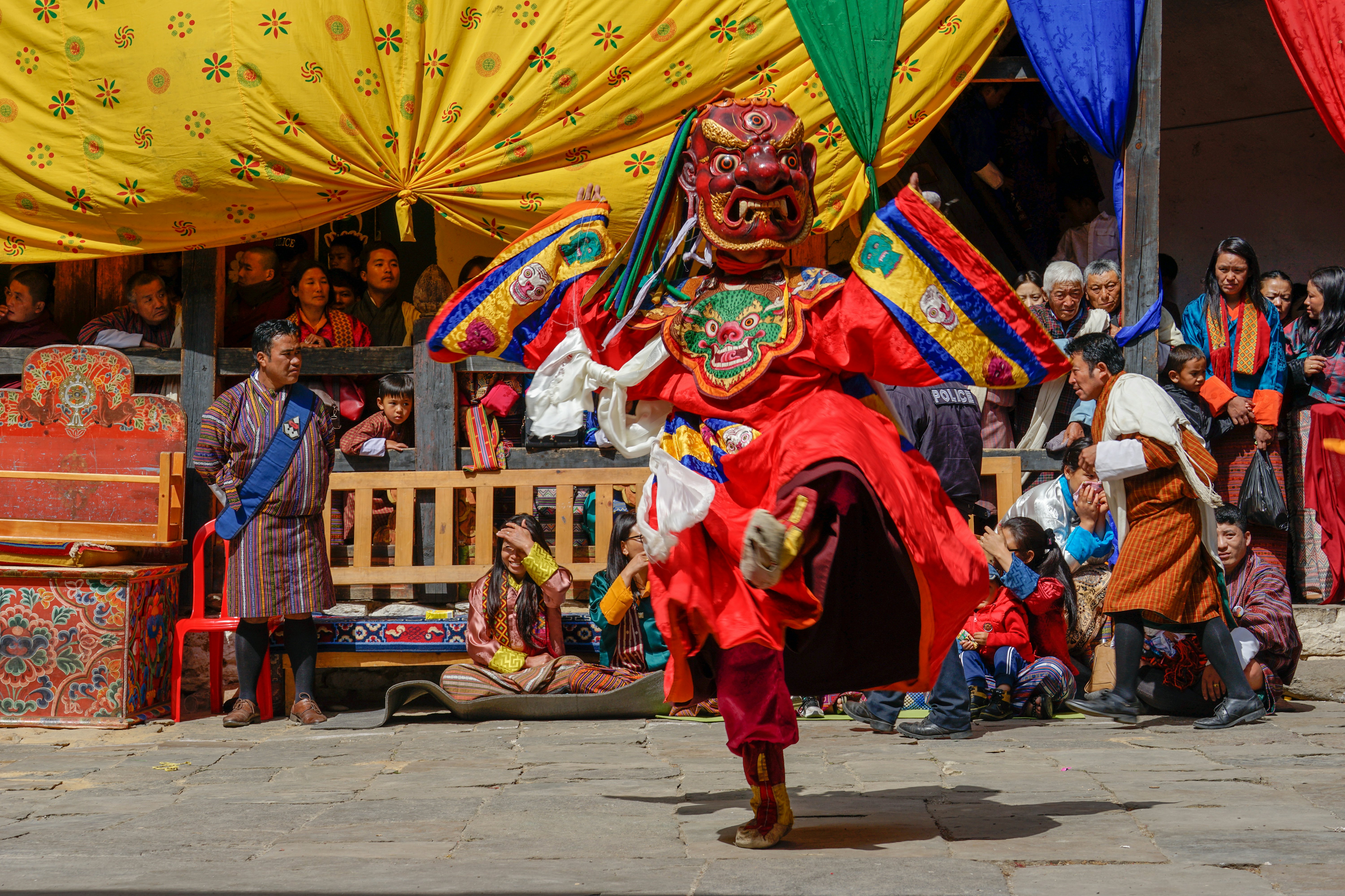 A dancer in a large red mask performs in front of a crowd.