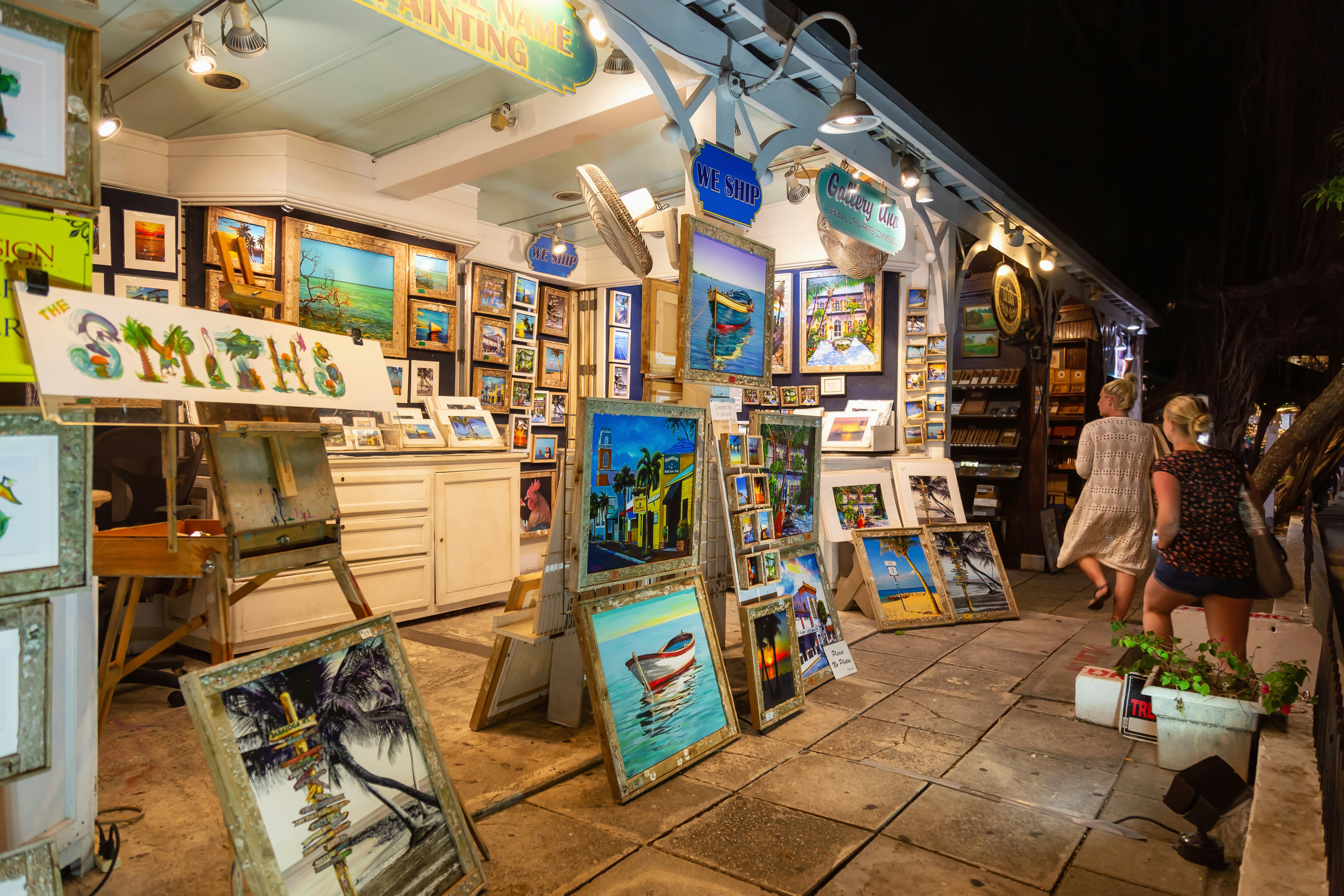 Paintings and other artwork are for sale at a stall on a street at night.
