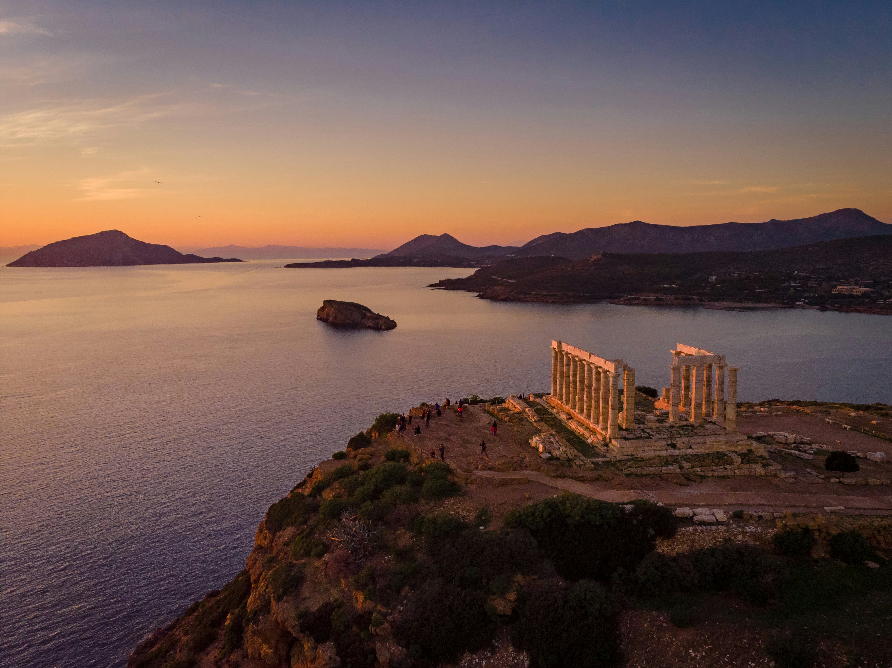 Sunset over the a temple's rising columns with water and mountains in the background