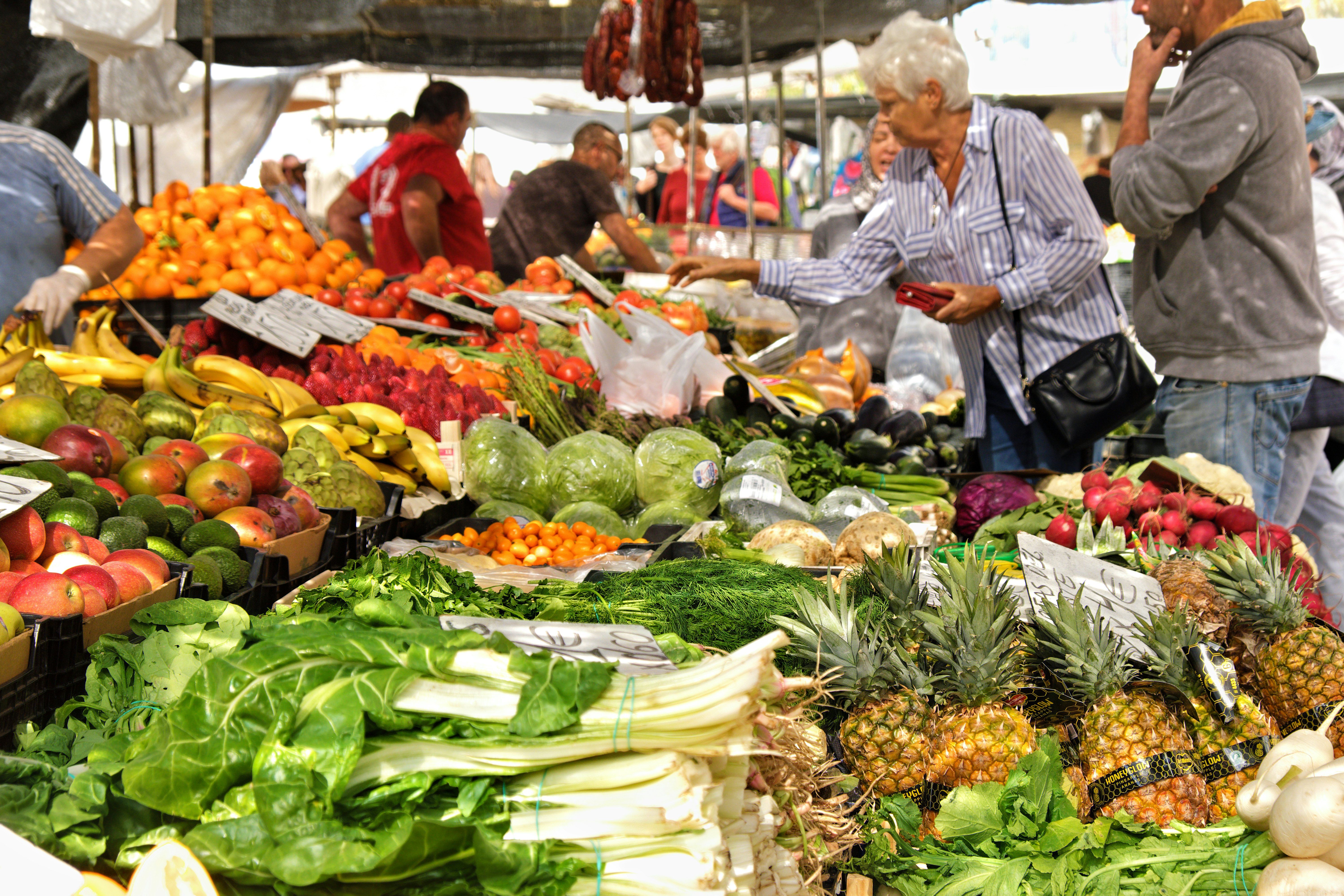 Shoppers look at fresh fruits and vegetables displayed at a market in Spain. Pineapples, oranges, mangos and leafy greens are among the produce available.