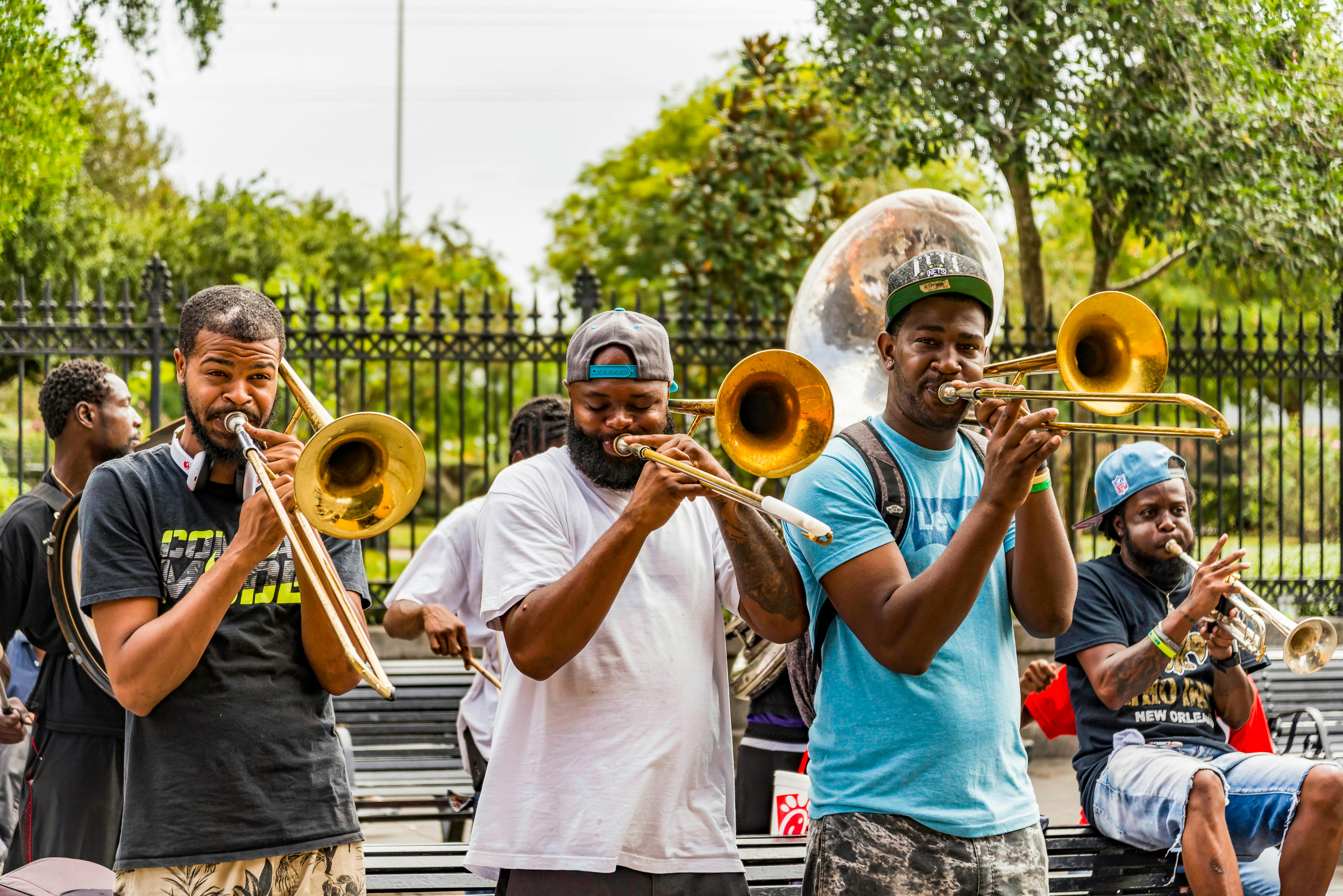 Men play trombones on a street in front of a city park.