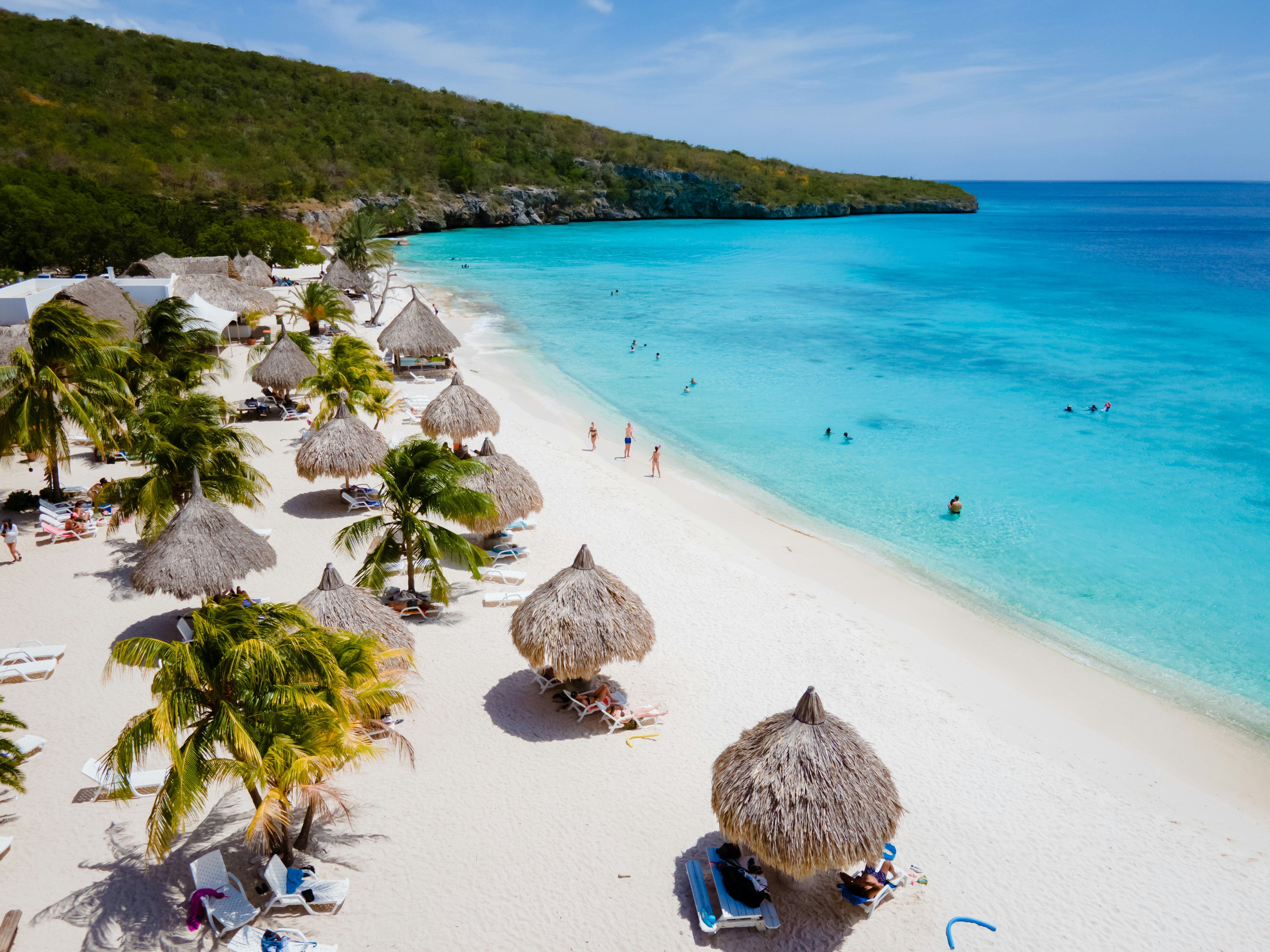 beach chairs under umbrellas on white sand with clear blue water