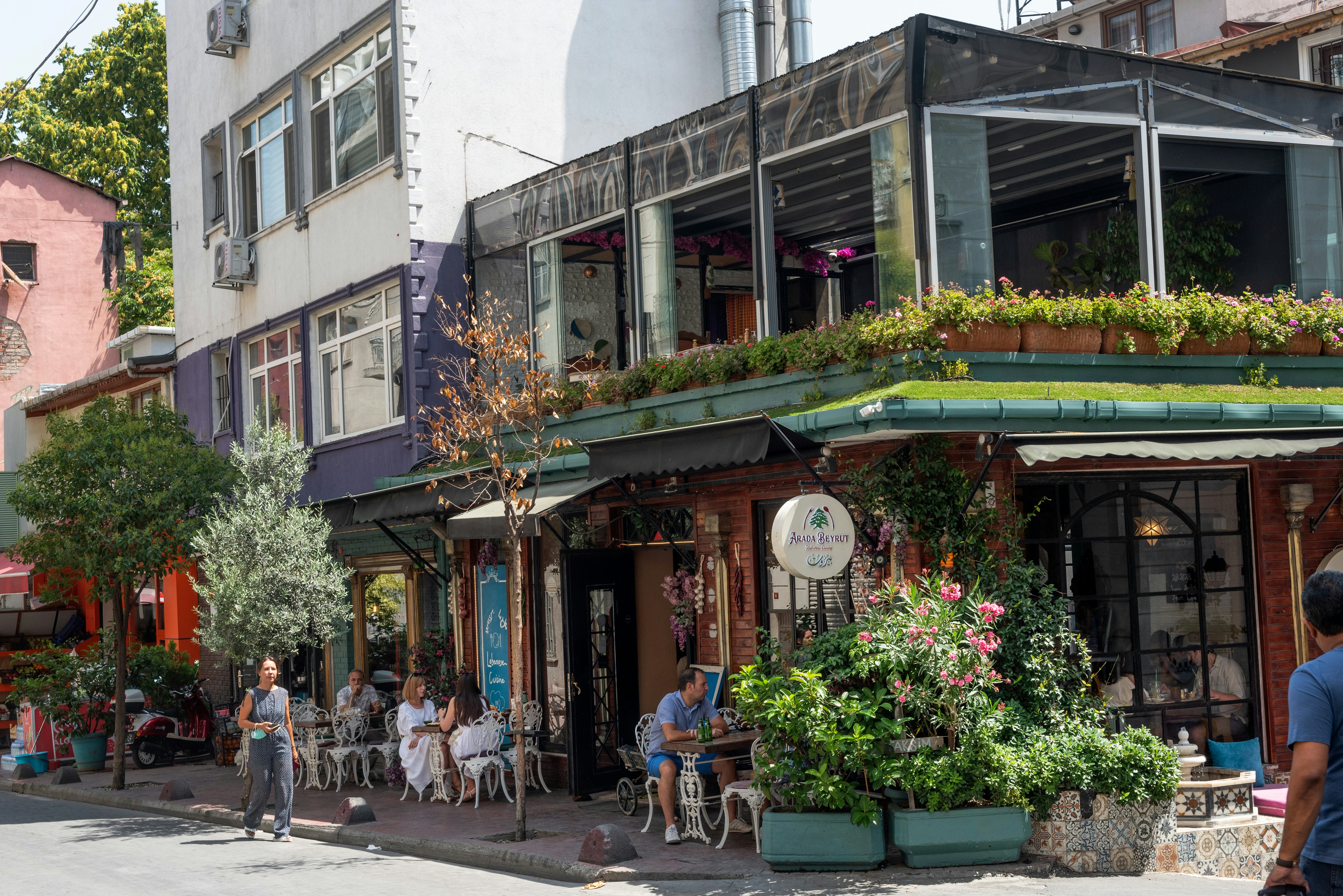 People sit outside a cafe on a corner in a street.
