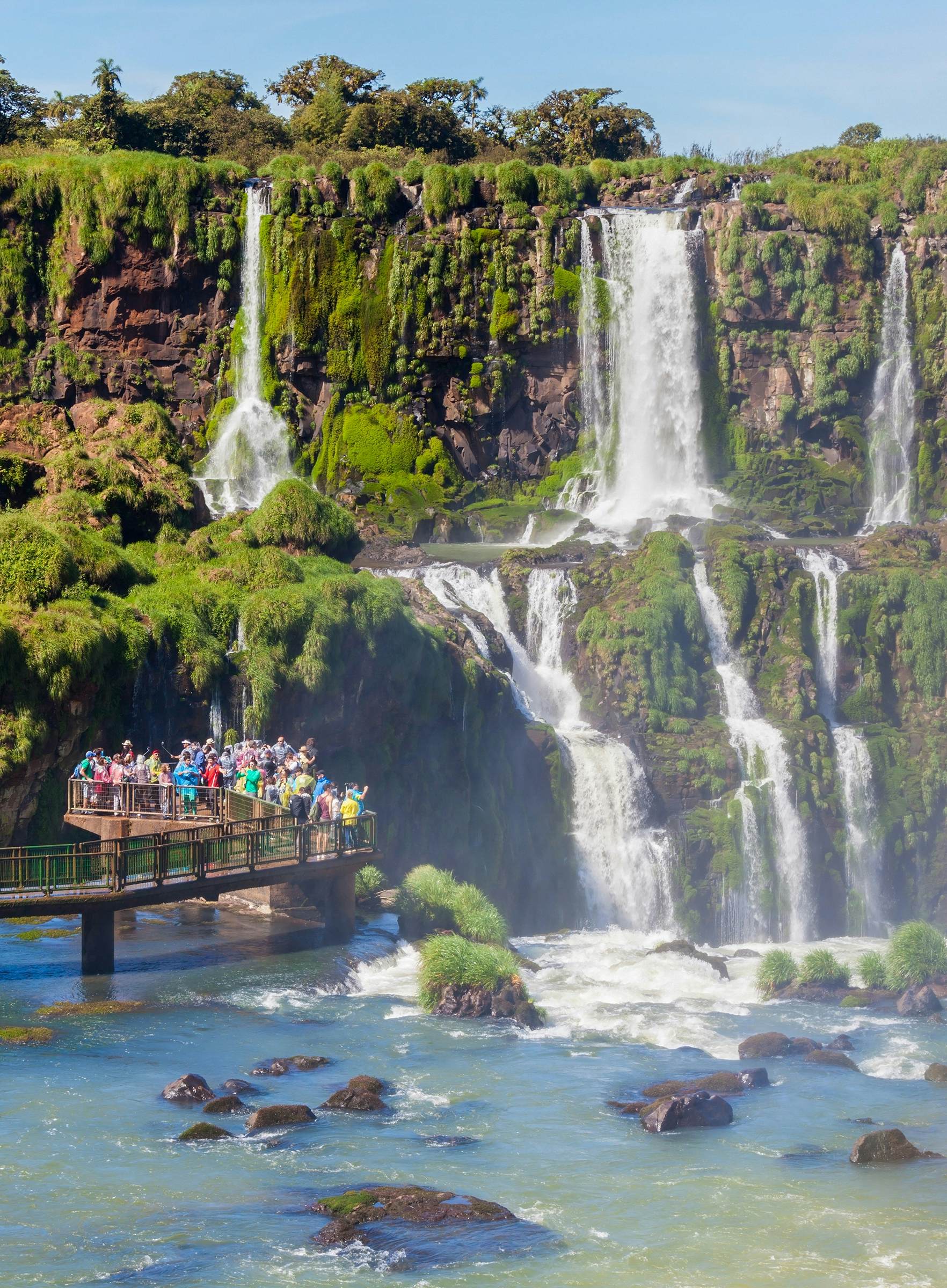 People stand on a platform at the base of a large series of waterfalls.