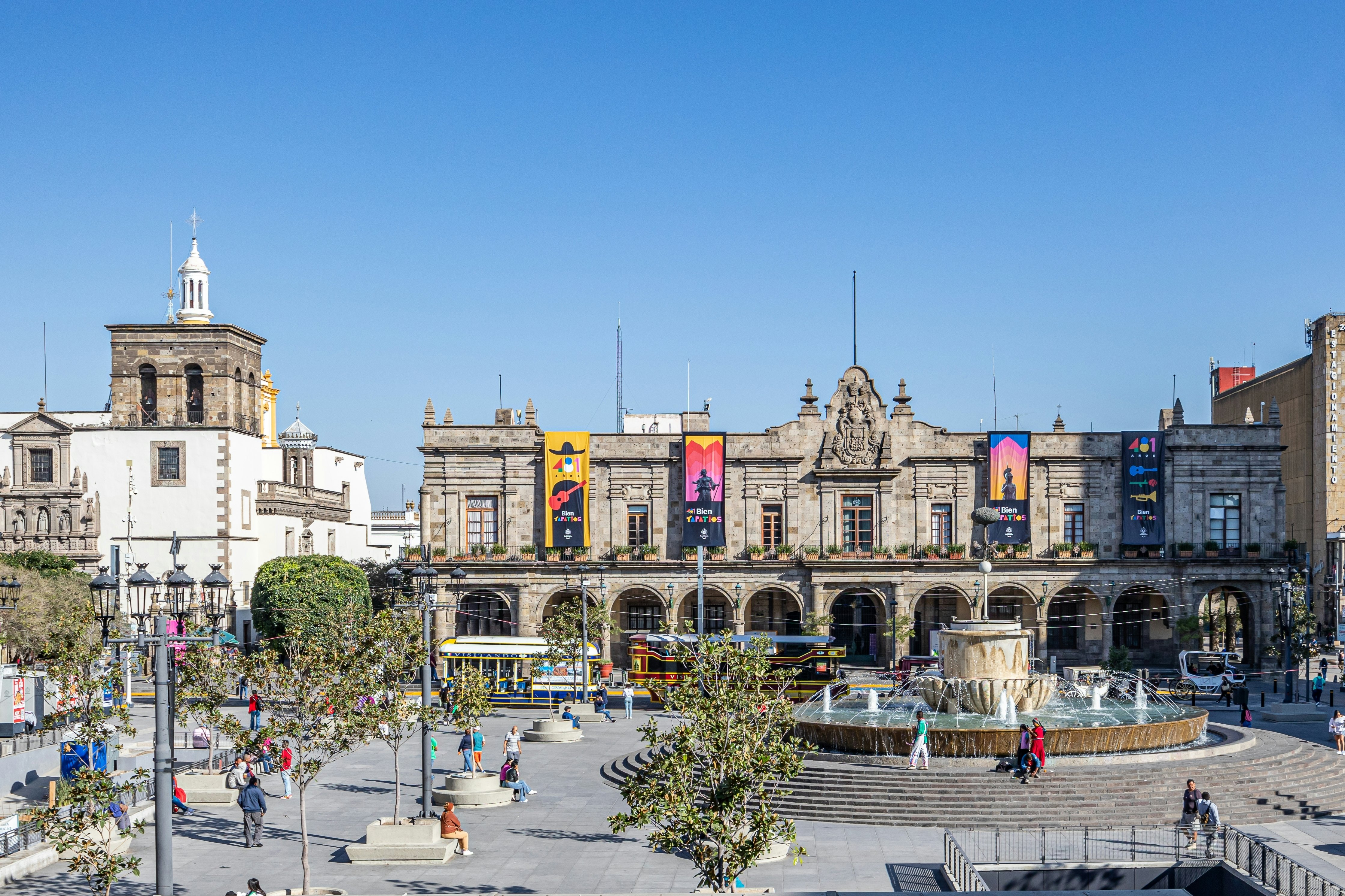 A plaza with fountain in the middle and people walking around