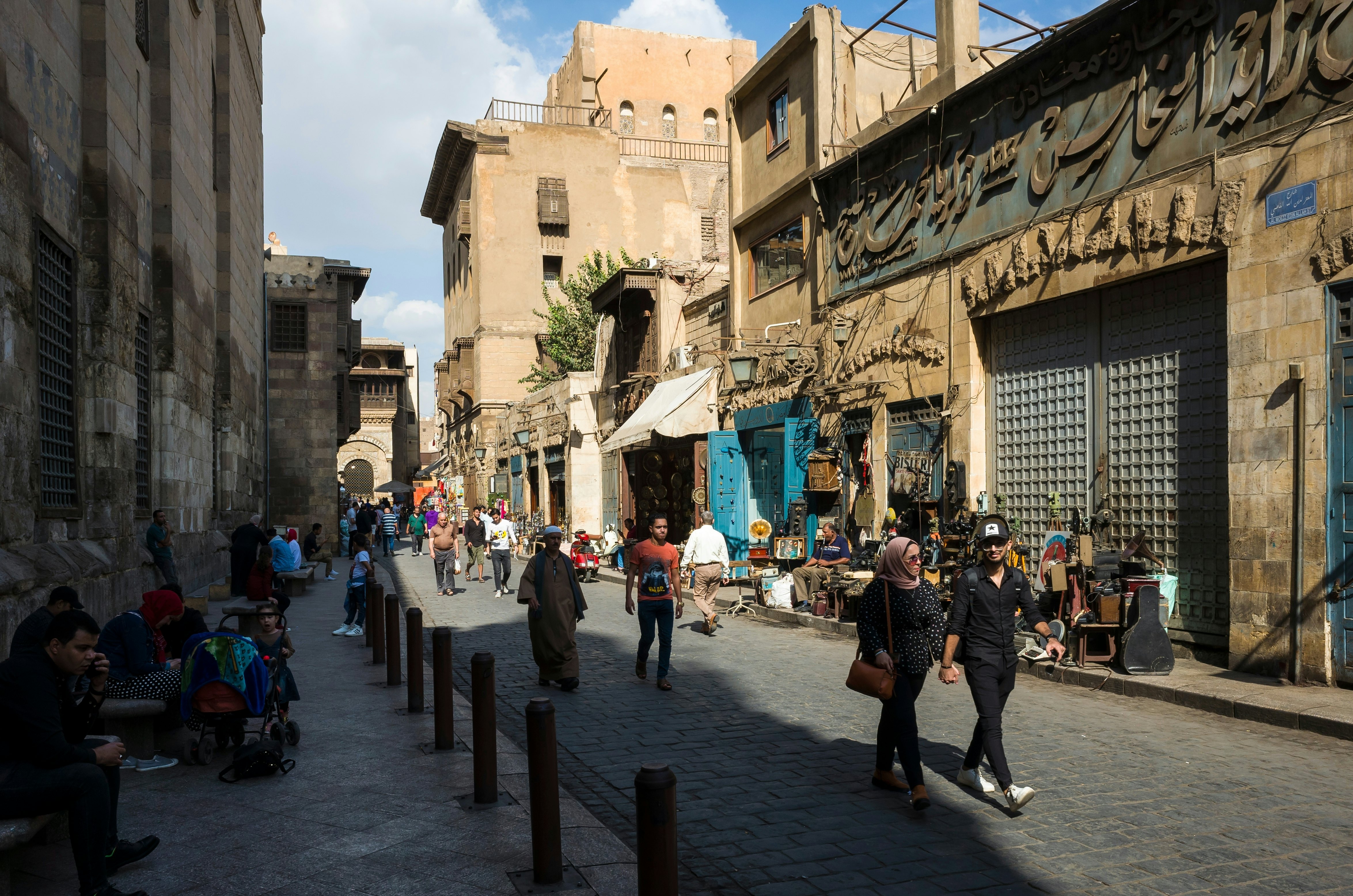 People on a pedestrian street lined with buildings that have Arabic writing on them