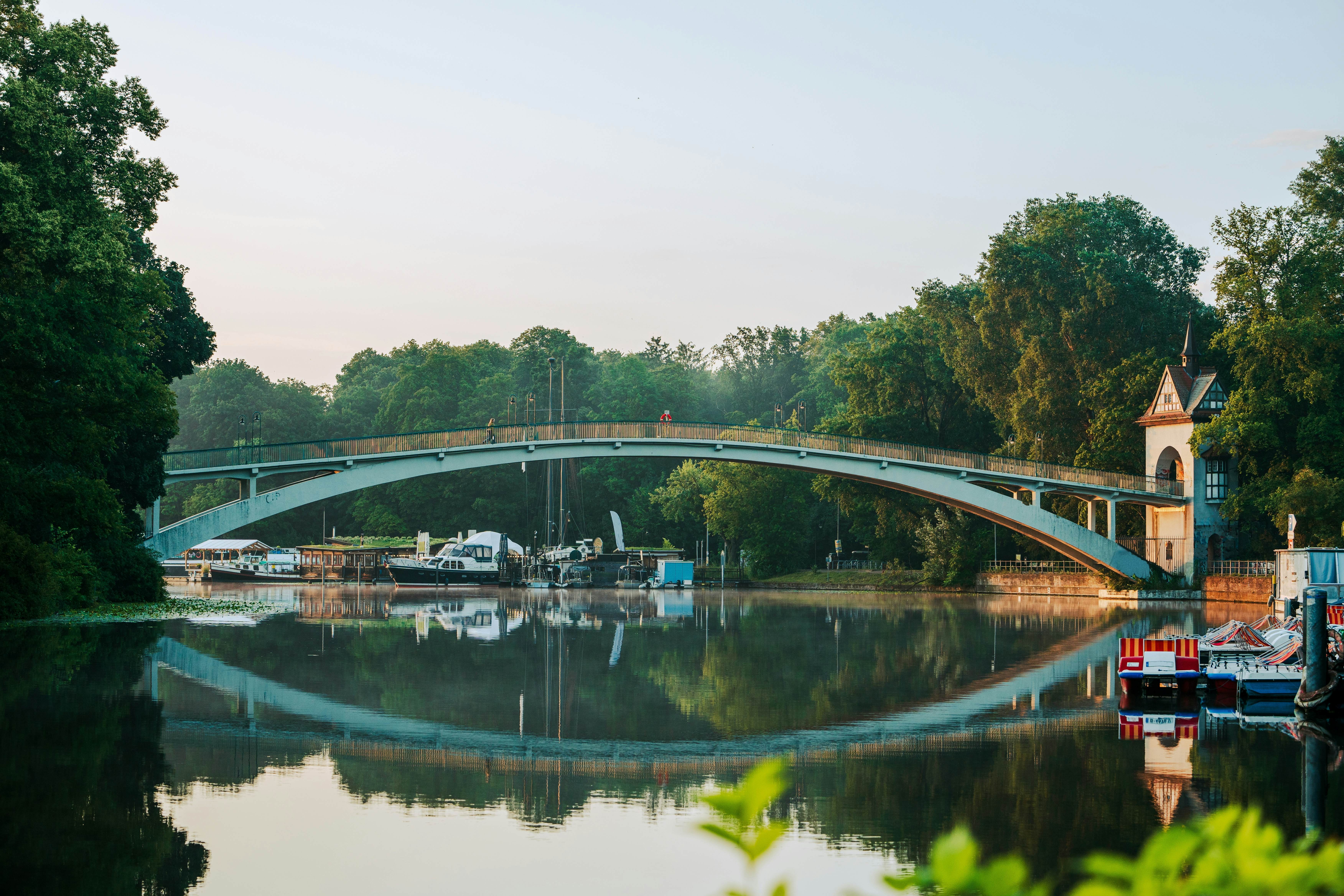 A river with boats is crossed by a bridge that is reflected in the water.