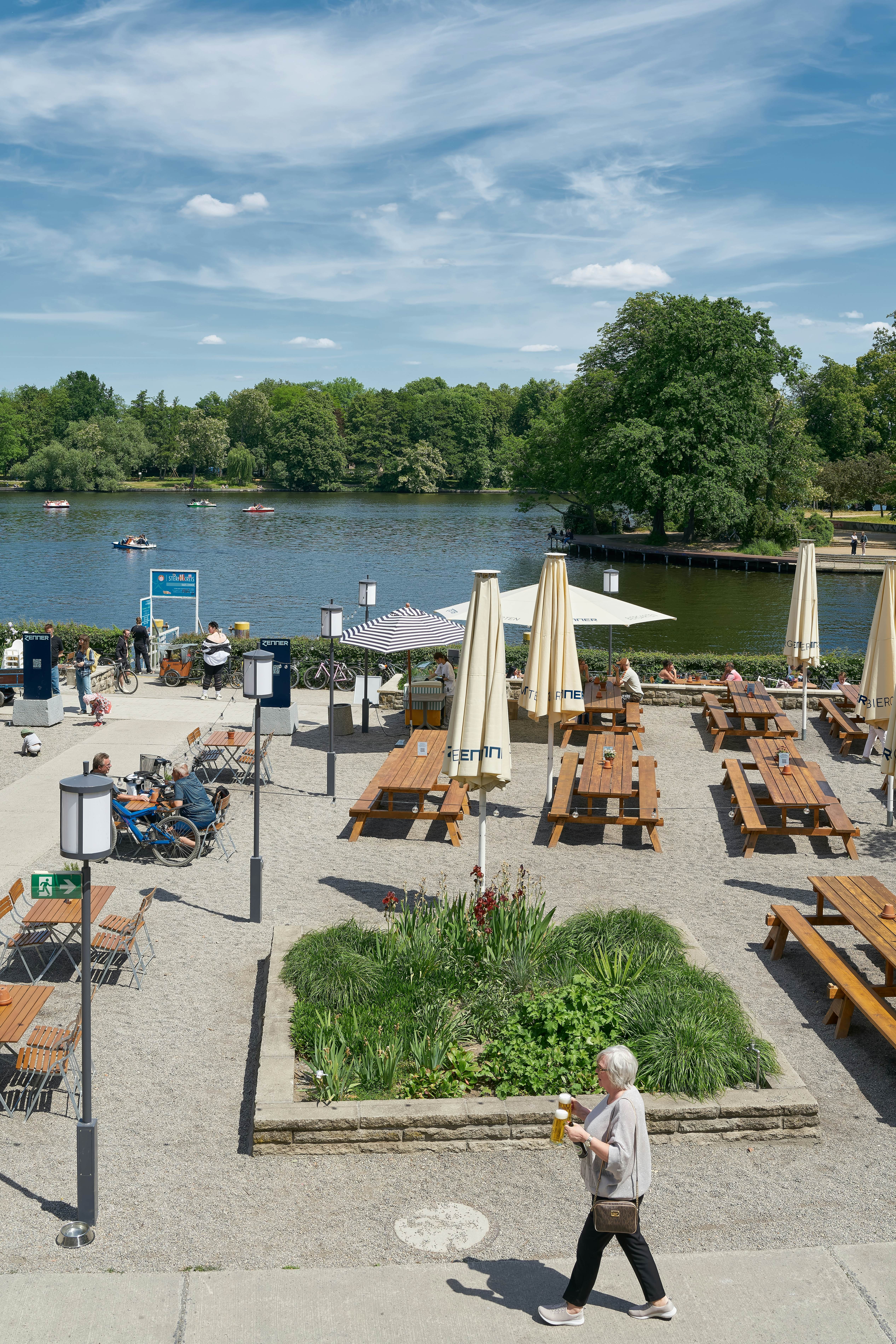 Picnic tables with closed umbrellas are set up by a riverbank.