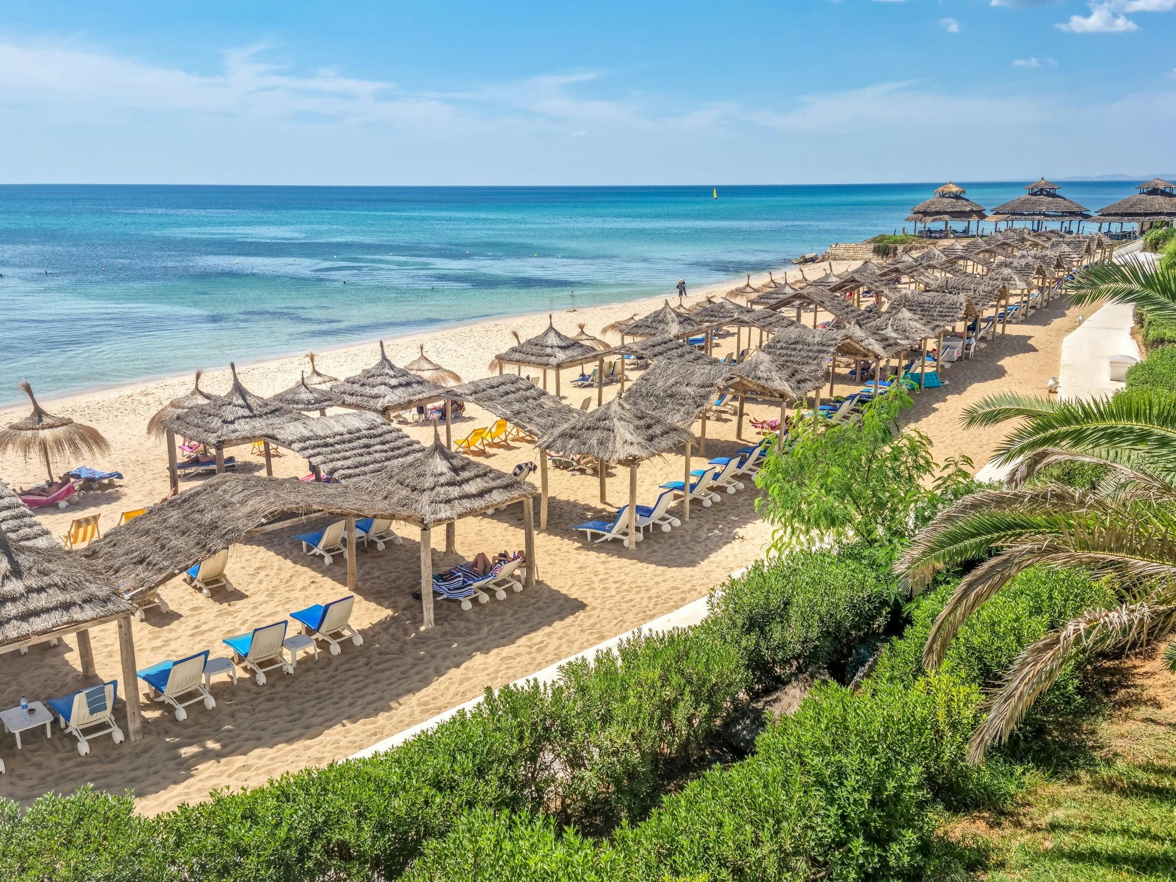 Palm canopies shade sun loungers on a beach in Hammamet, Tunisia.