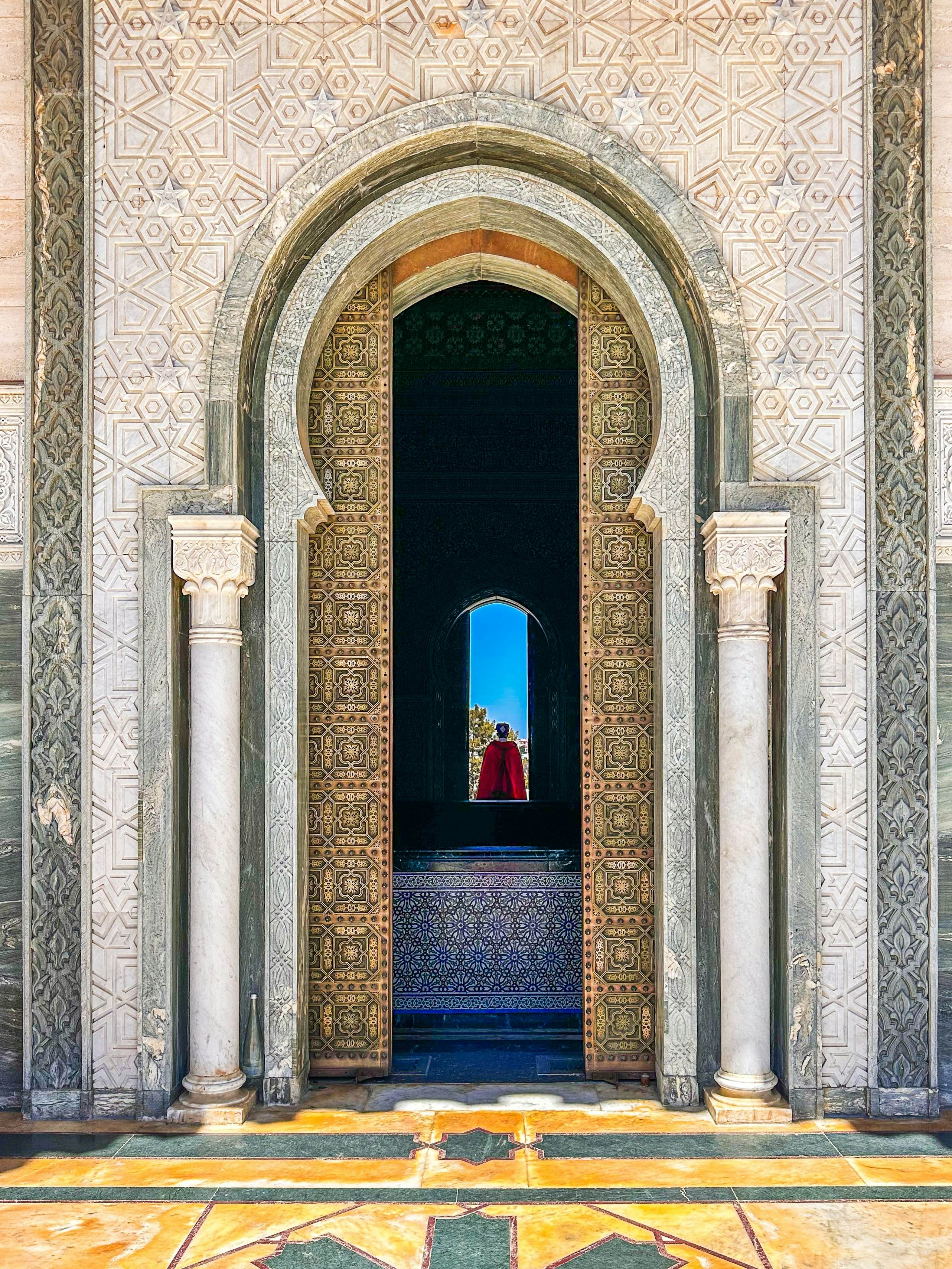 A doorway with carvings and columns leads to a dark passageway; a person is in the doorway at the other end.
