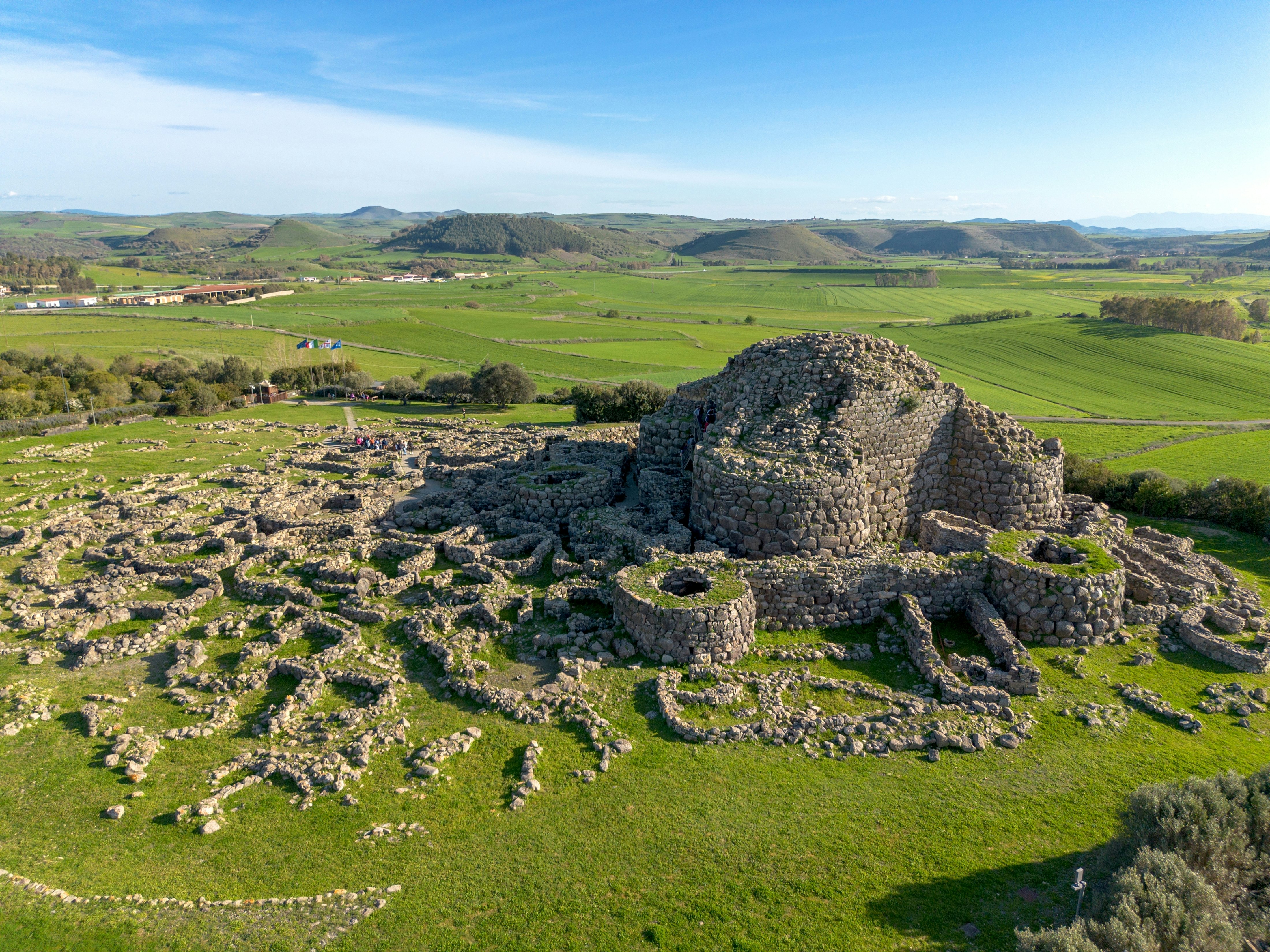 Aerial view of ancient ruins made of stone amid green grass on a sunny day.