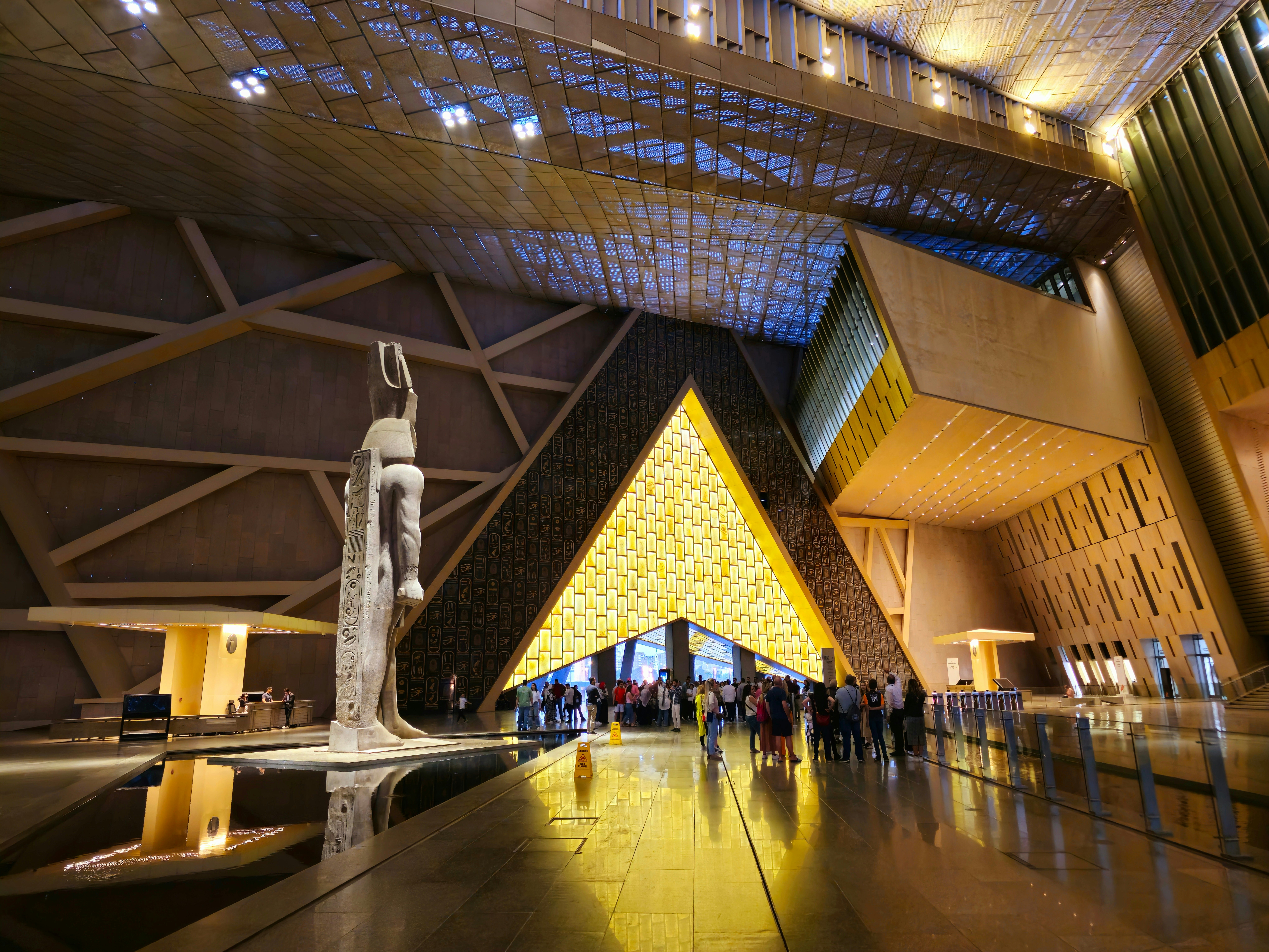 A museum hall with a large statue and an entrance with lighting shaped like a pyramid.
