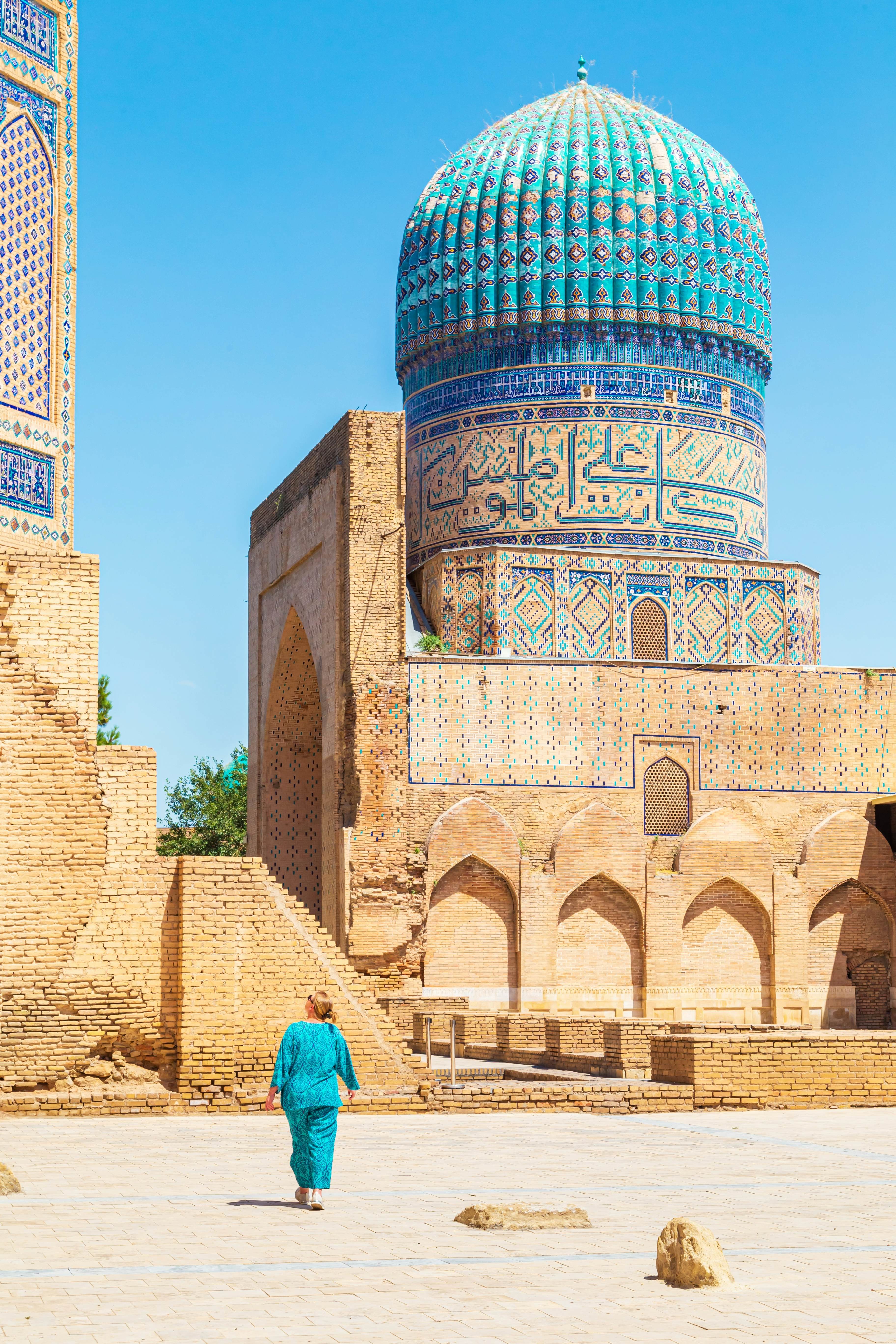 Woman in blue traditional dress in the courtyard of an elaborately decorated mosque.