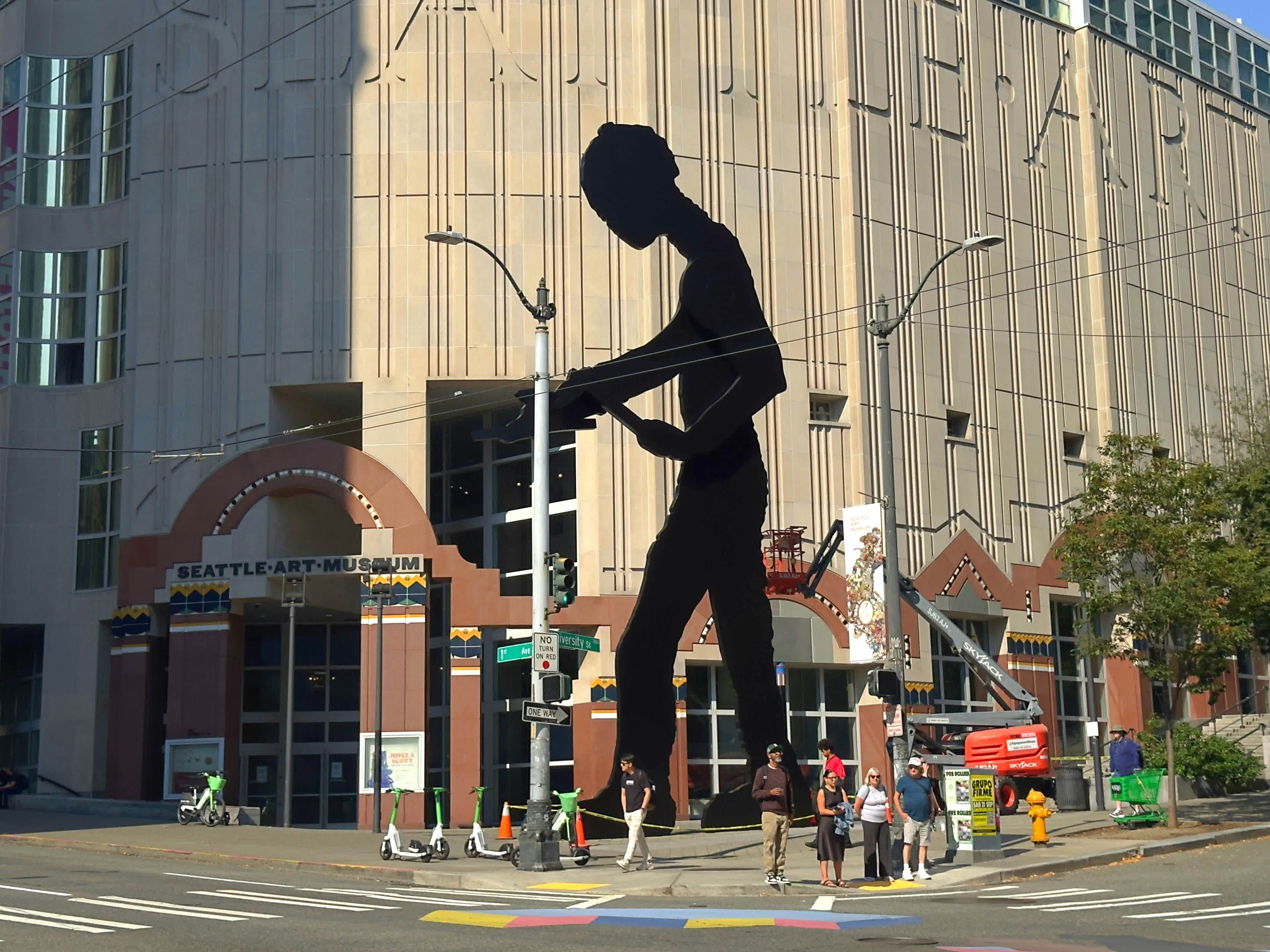 A huge artwork of a figure in silhouette adorns a building on a street in a city.