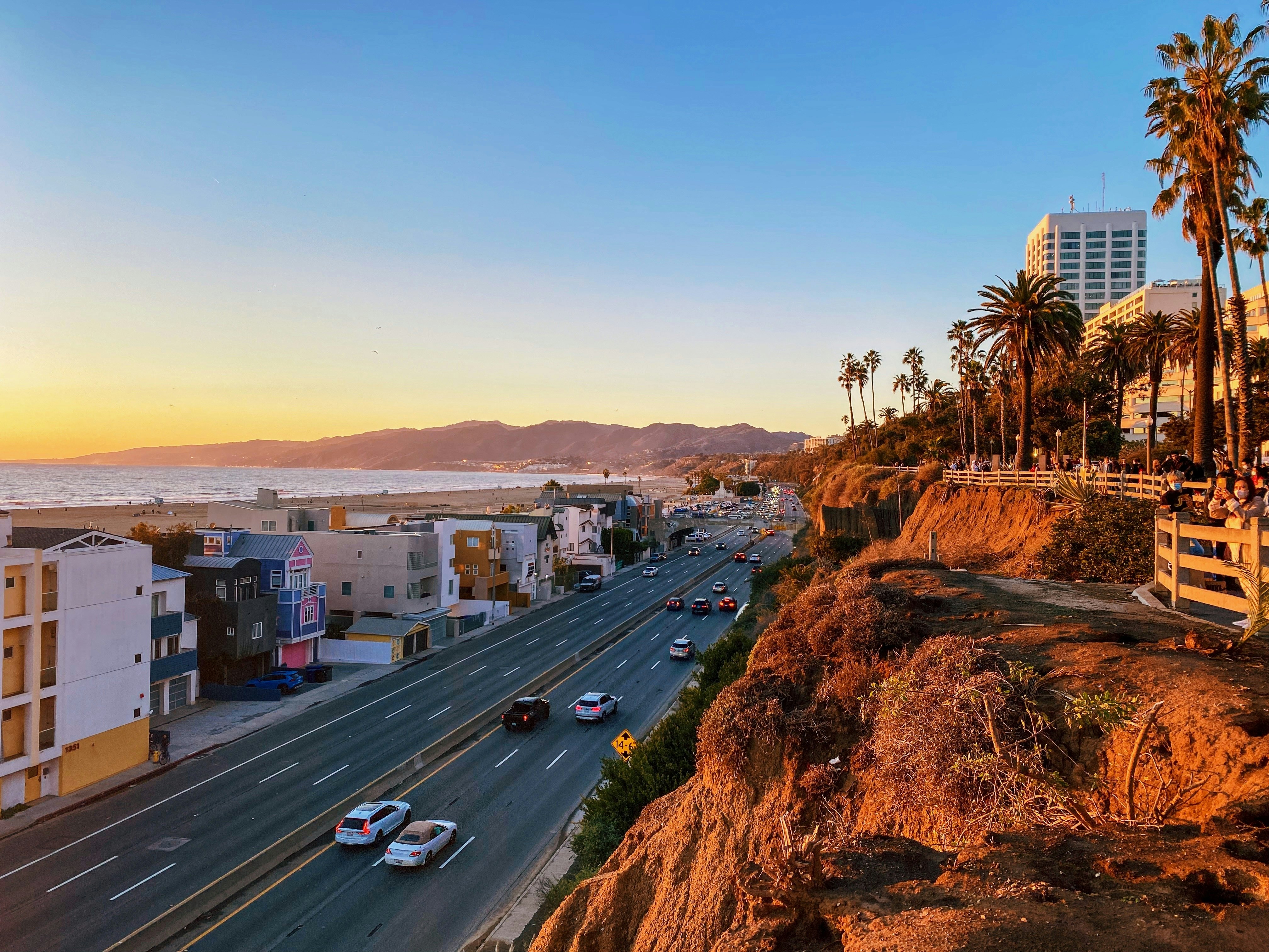 A coastal highway at dusk. Beach cliffs and high rise hotels are on the right, while the left hand side is beachside apartments.