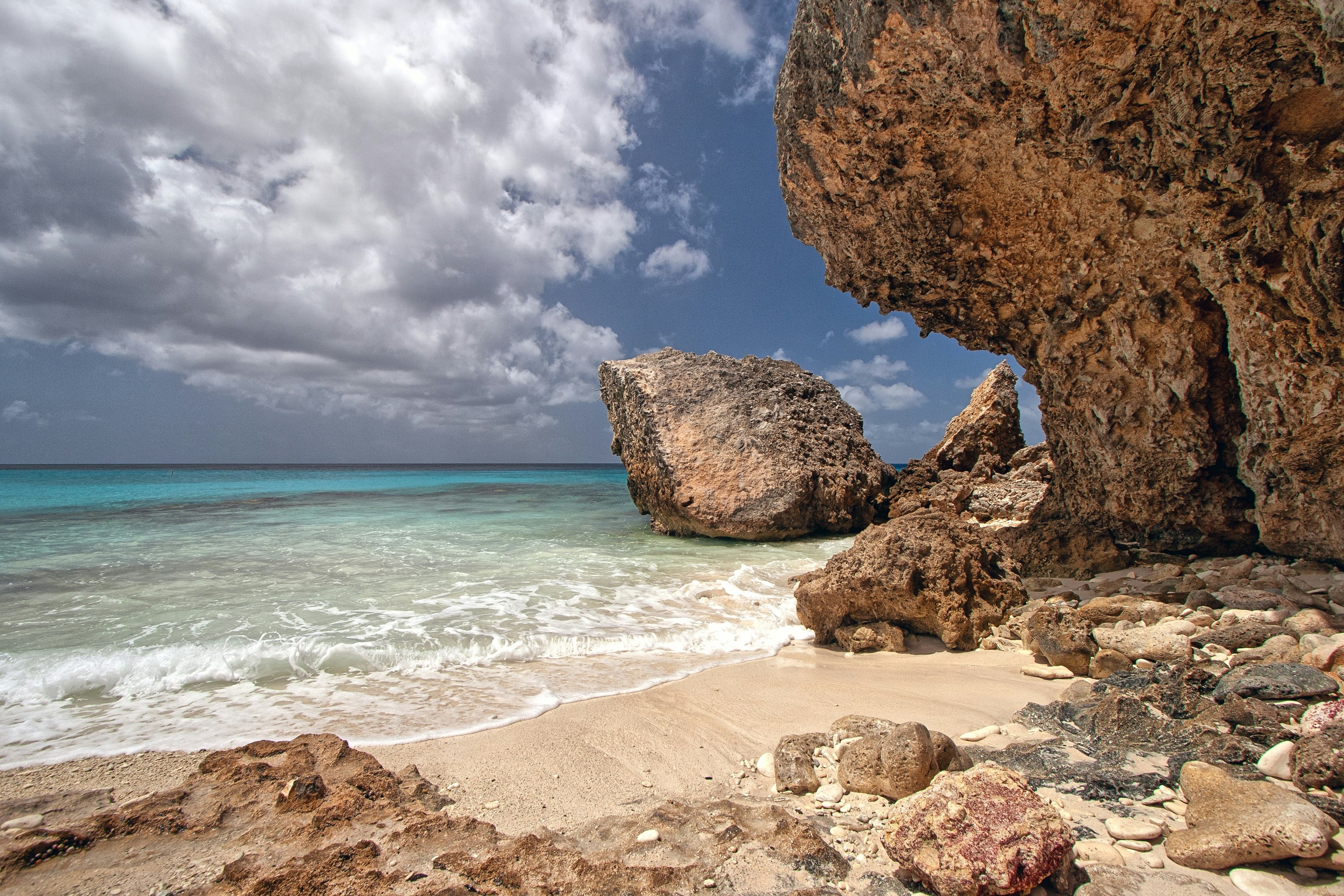 A rocky beach is framed by cliffs and boulders in a tropical location.