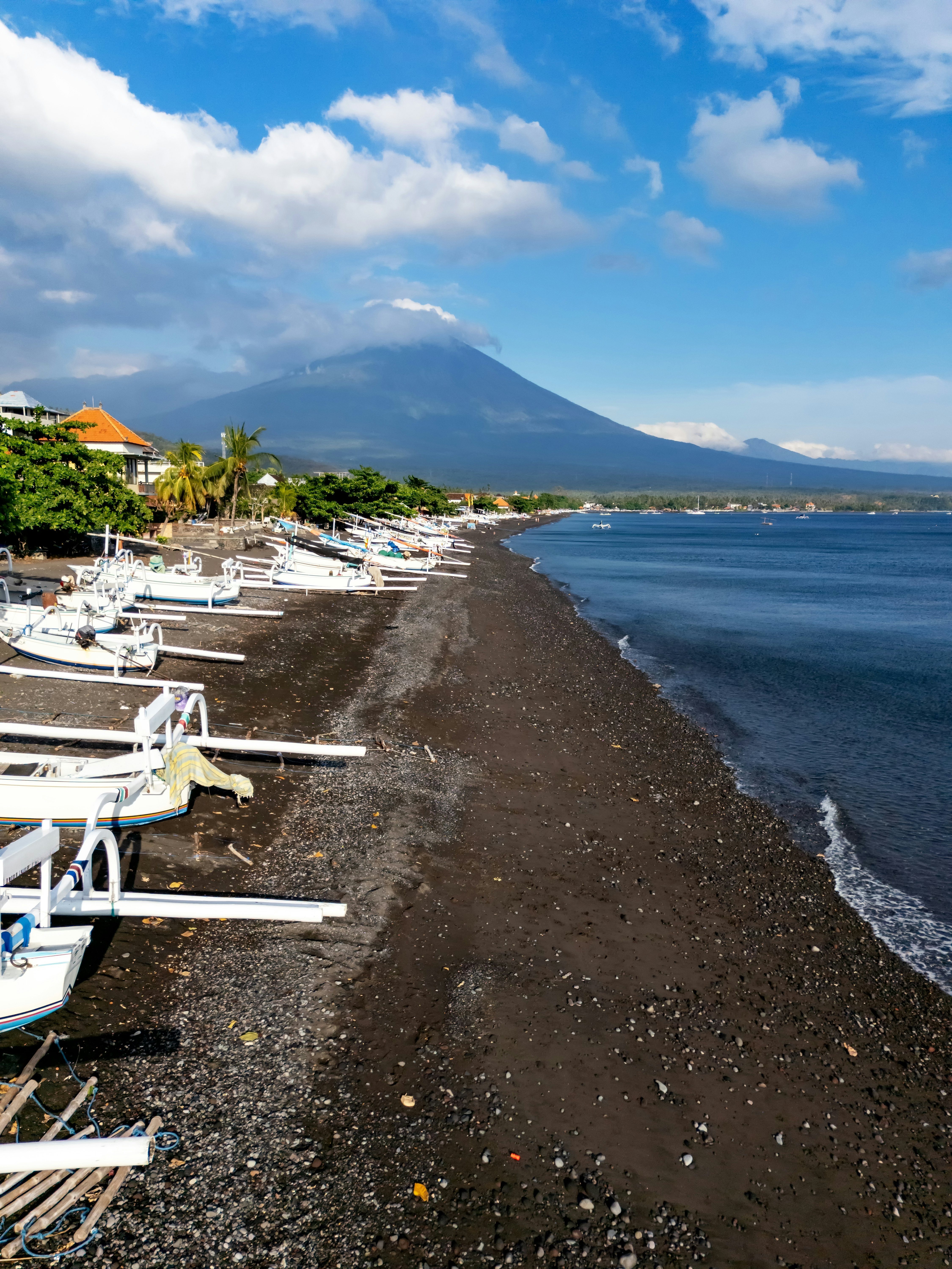 A black sand beach lined with white canoe boats and an inactive volcano rising in the background