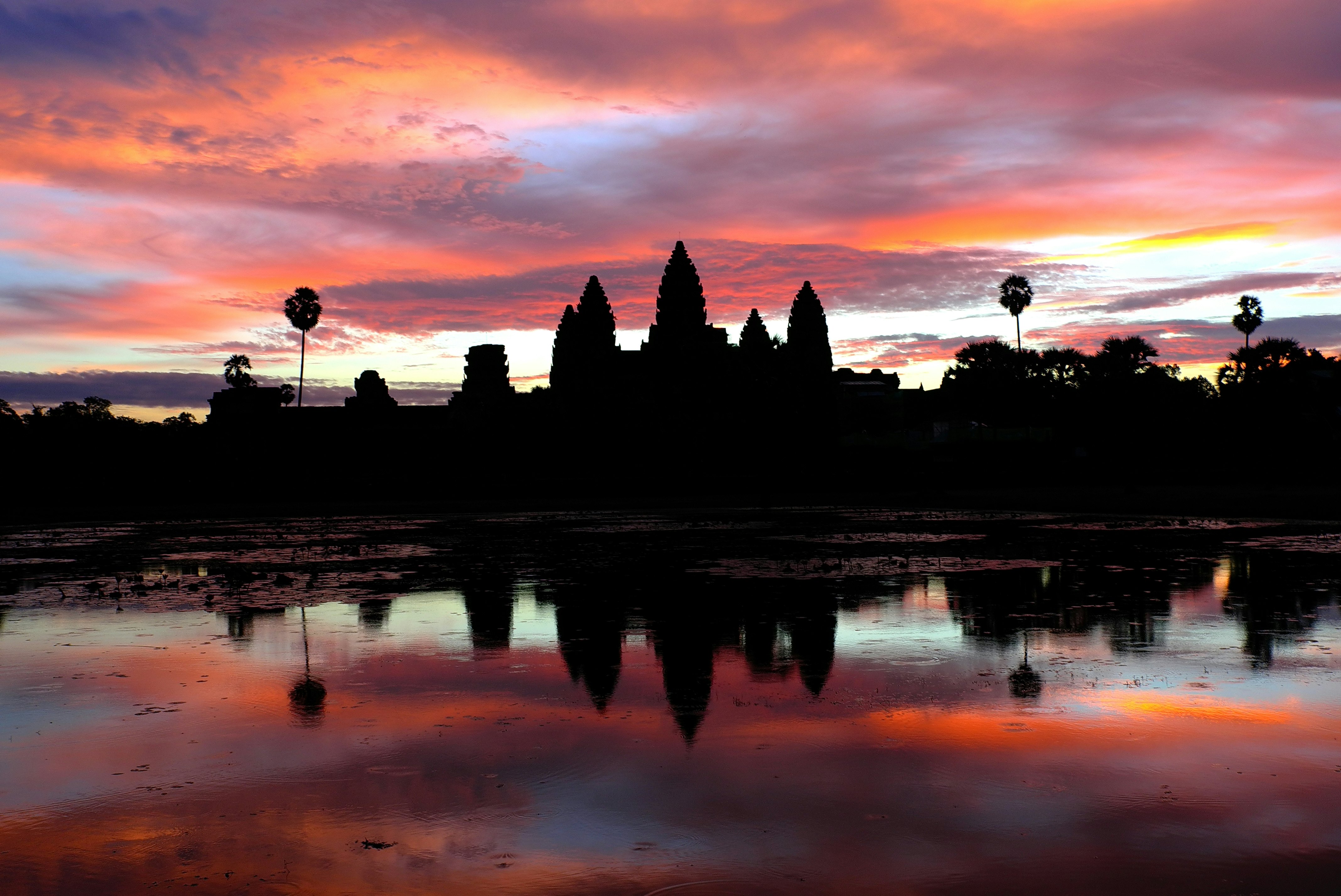 An ornate temple is silhouetted against a gorgeous sky showing pink, purple and orange tones at sunrise.