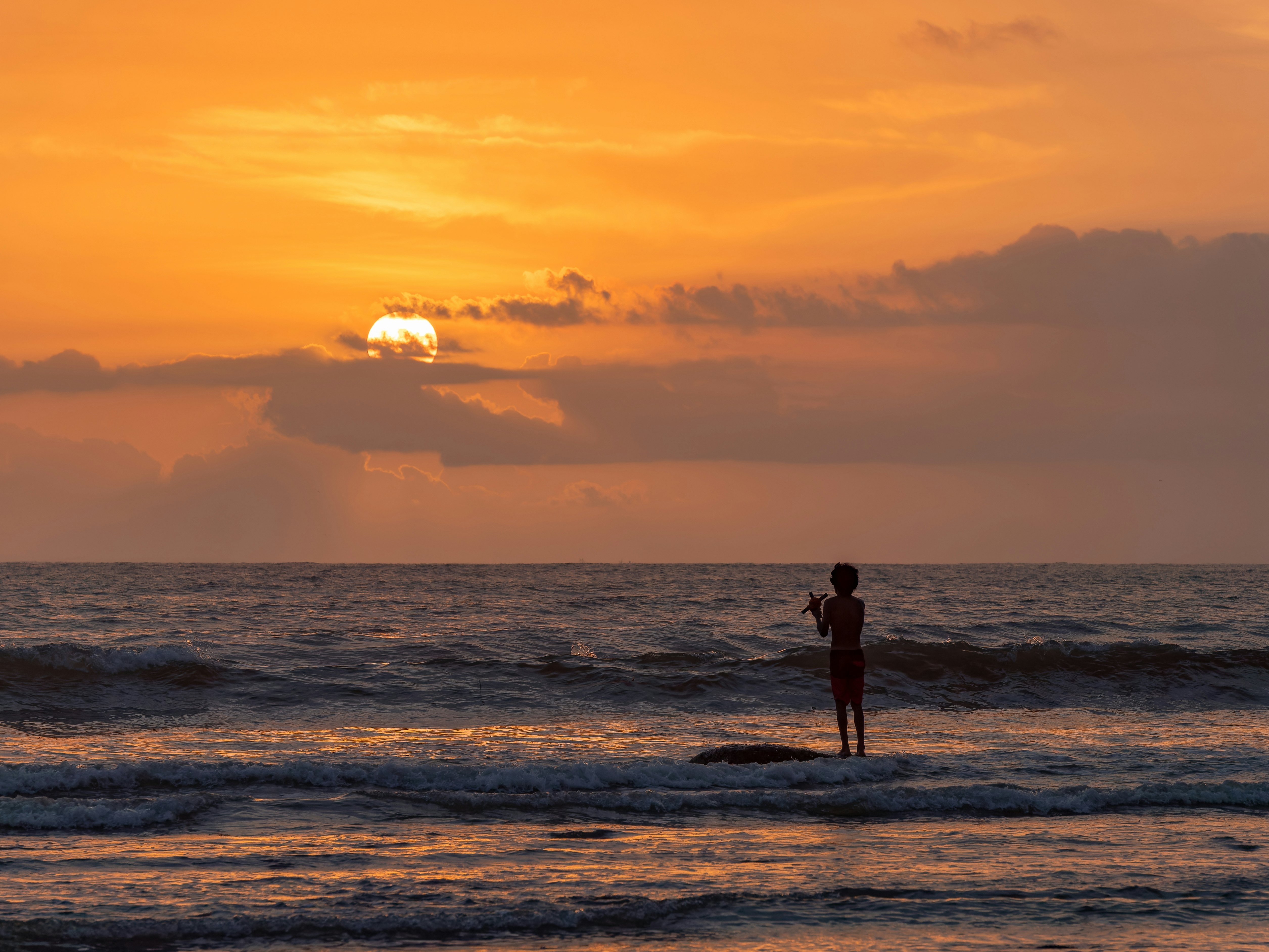 A fisher on a beach at sunset as waves roll up on the shore