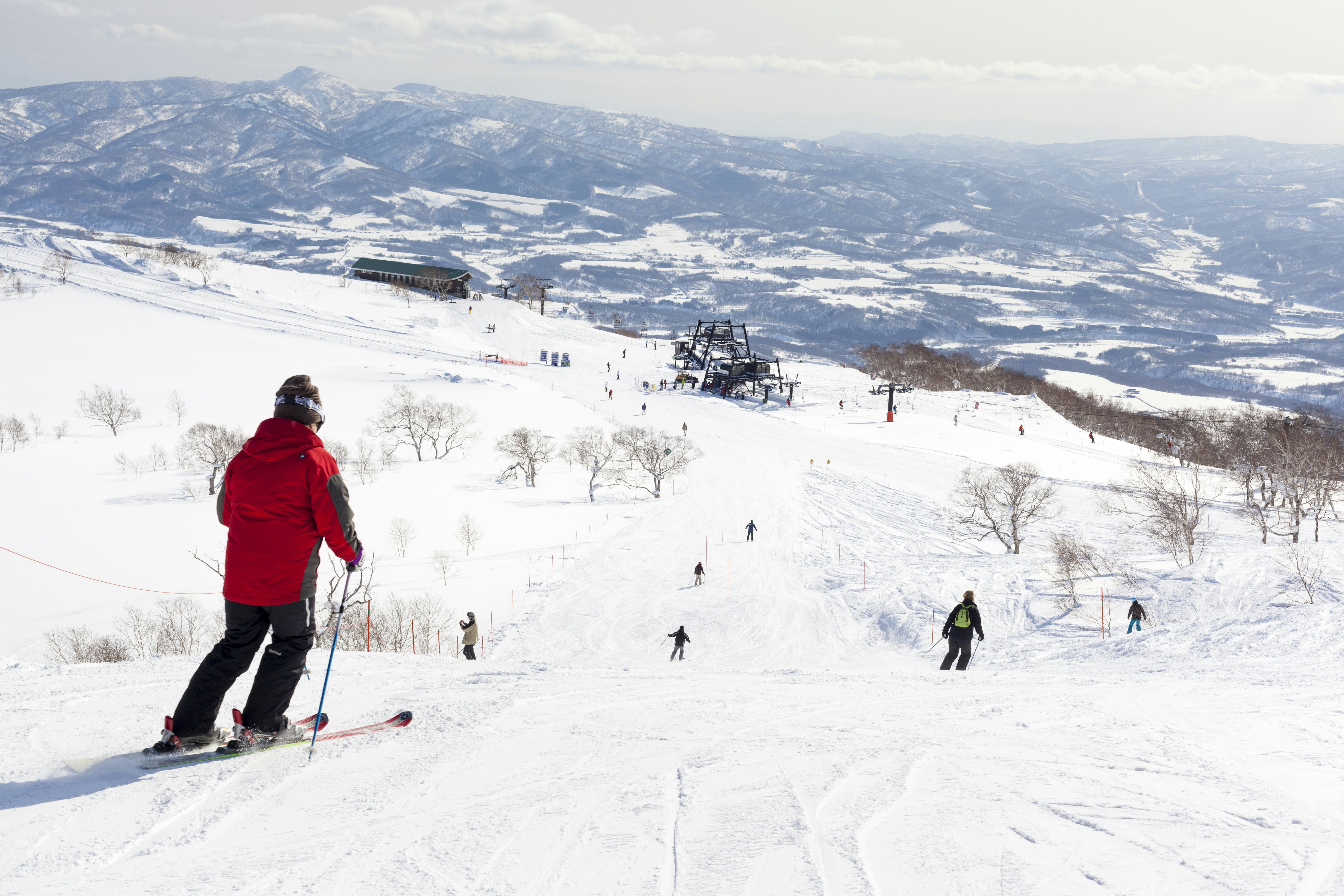 Skiers skiing down groomed slopes with low mountains in the distance on a sunny day.