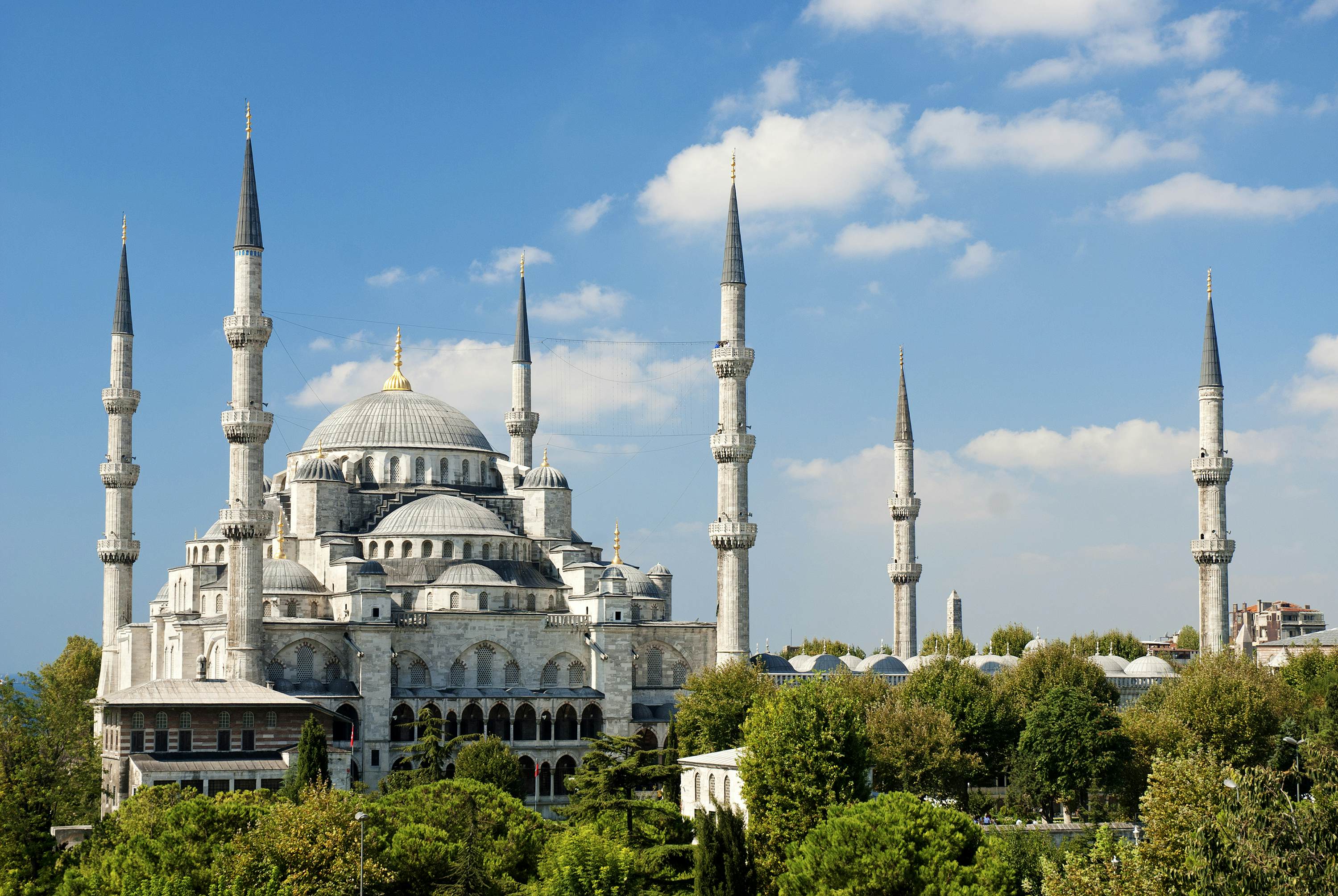 Exterior of a mosque with rounded roofs surrounded by pointed stone columns on a sunny day.
