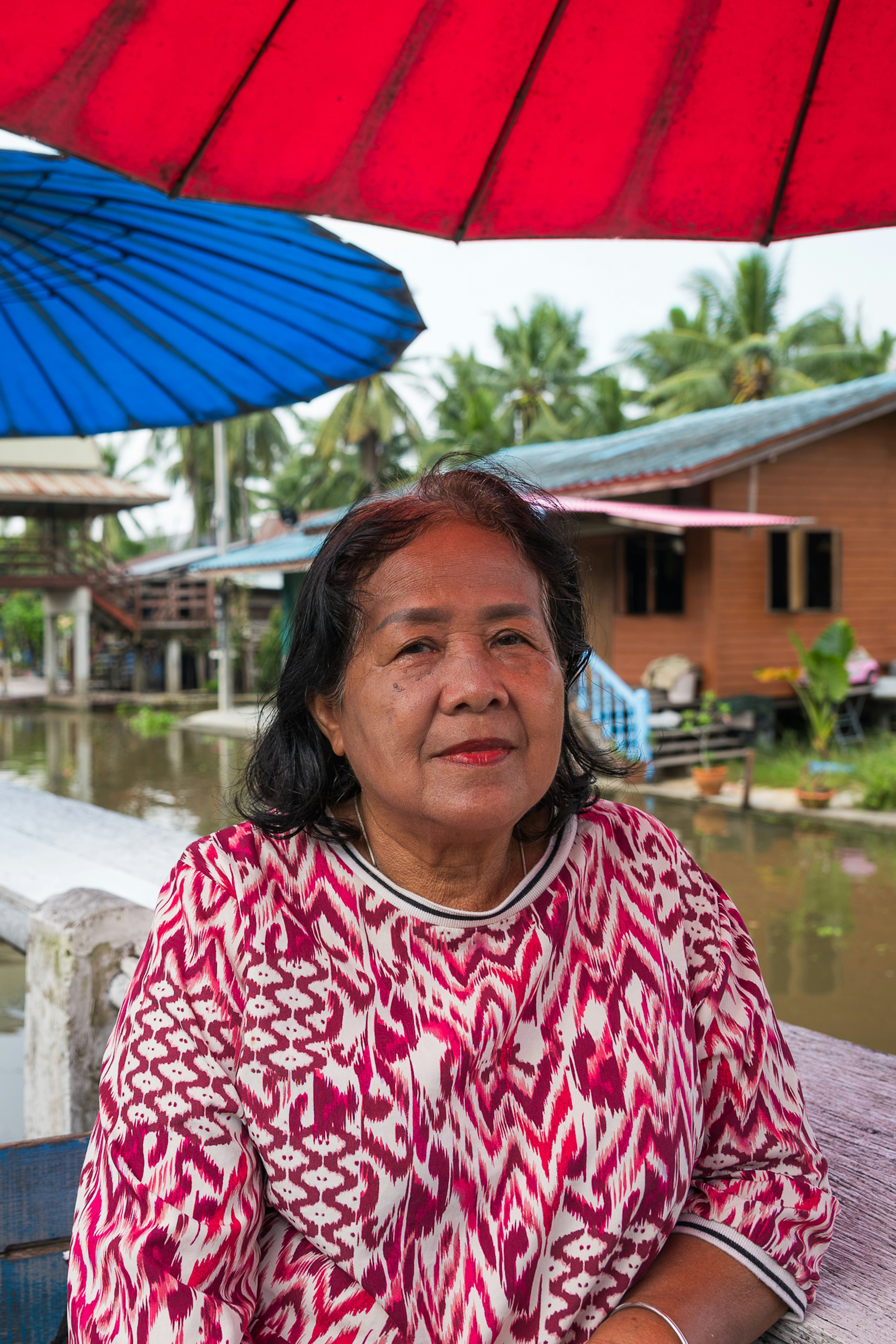 A woman in a brightly printed shirt looks into the camera aboard a boat in a canal.