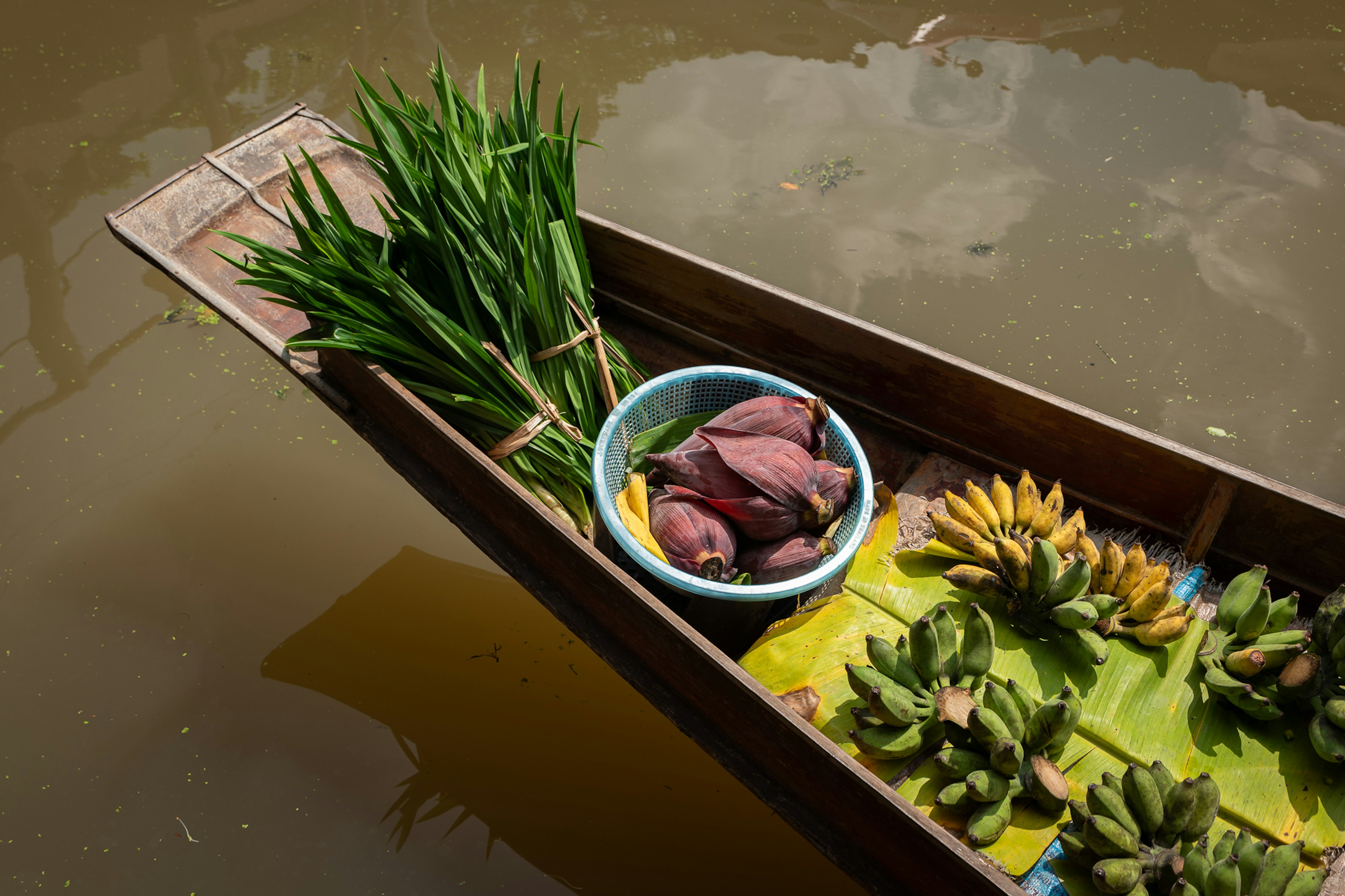 Fresh produce including pandan leaves and bananas is placed on a narrow boat, ready to be sold at a floating market.
