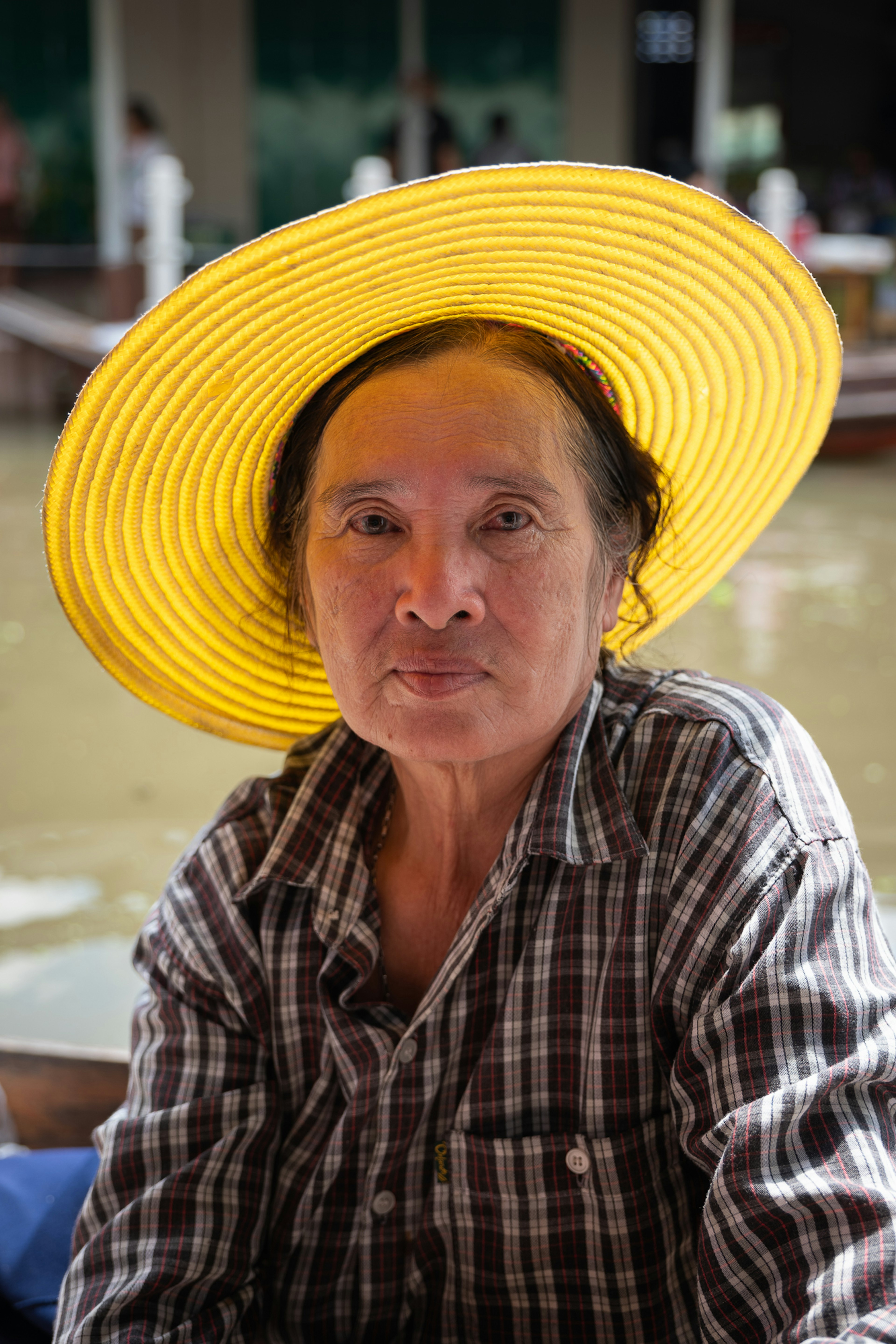 A close-up shot of a female vendor wearing a wide-brimmed hat at a floating market.
