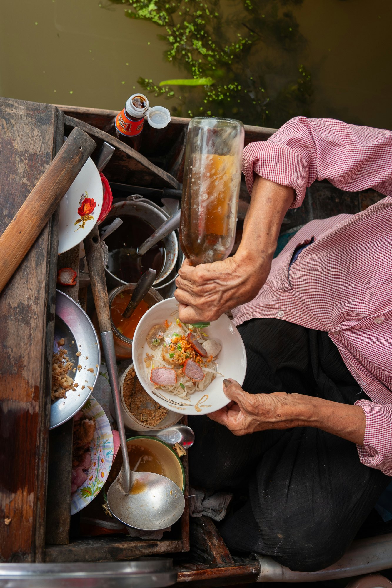 A close up of a female vendor preparing noodles on a small boat.