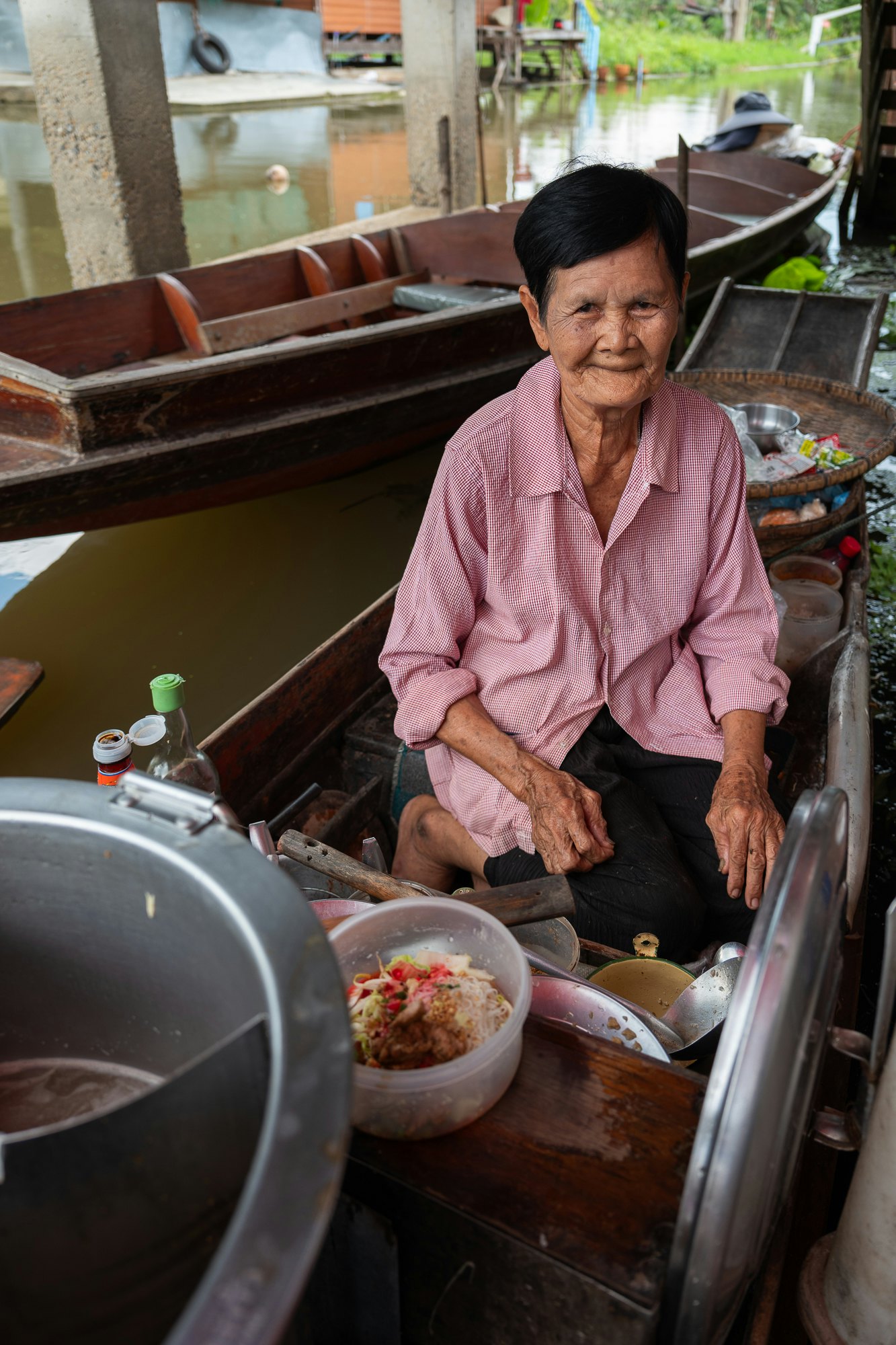 A female vendor on a boat, preparing food, smiles.