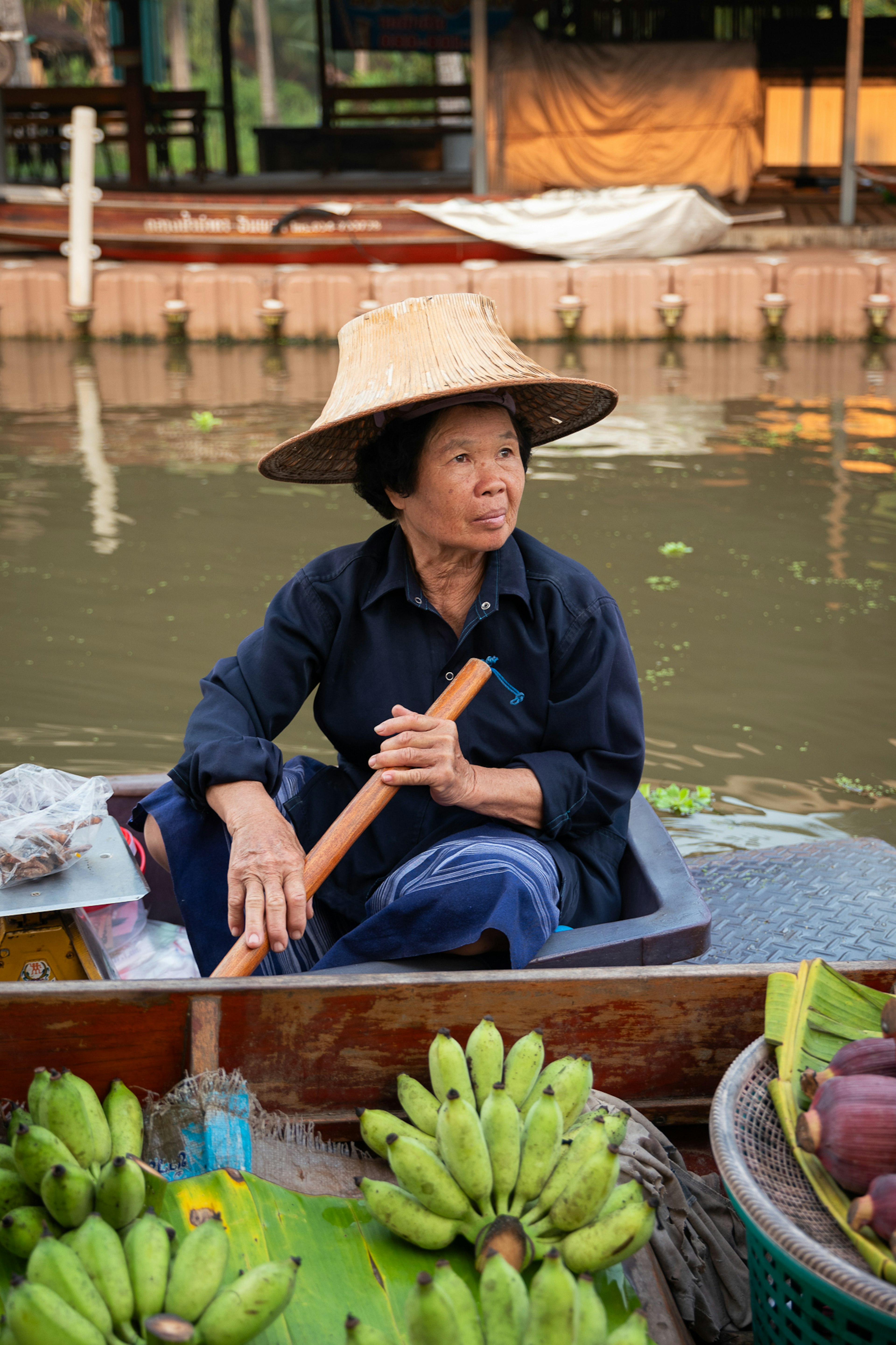 A local vendor wears a traditional hat made of nipa palm as she sells bananas in a boat at a floating market.