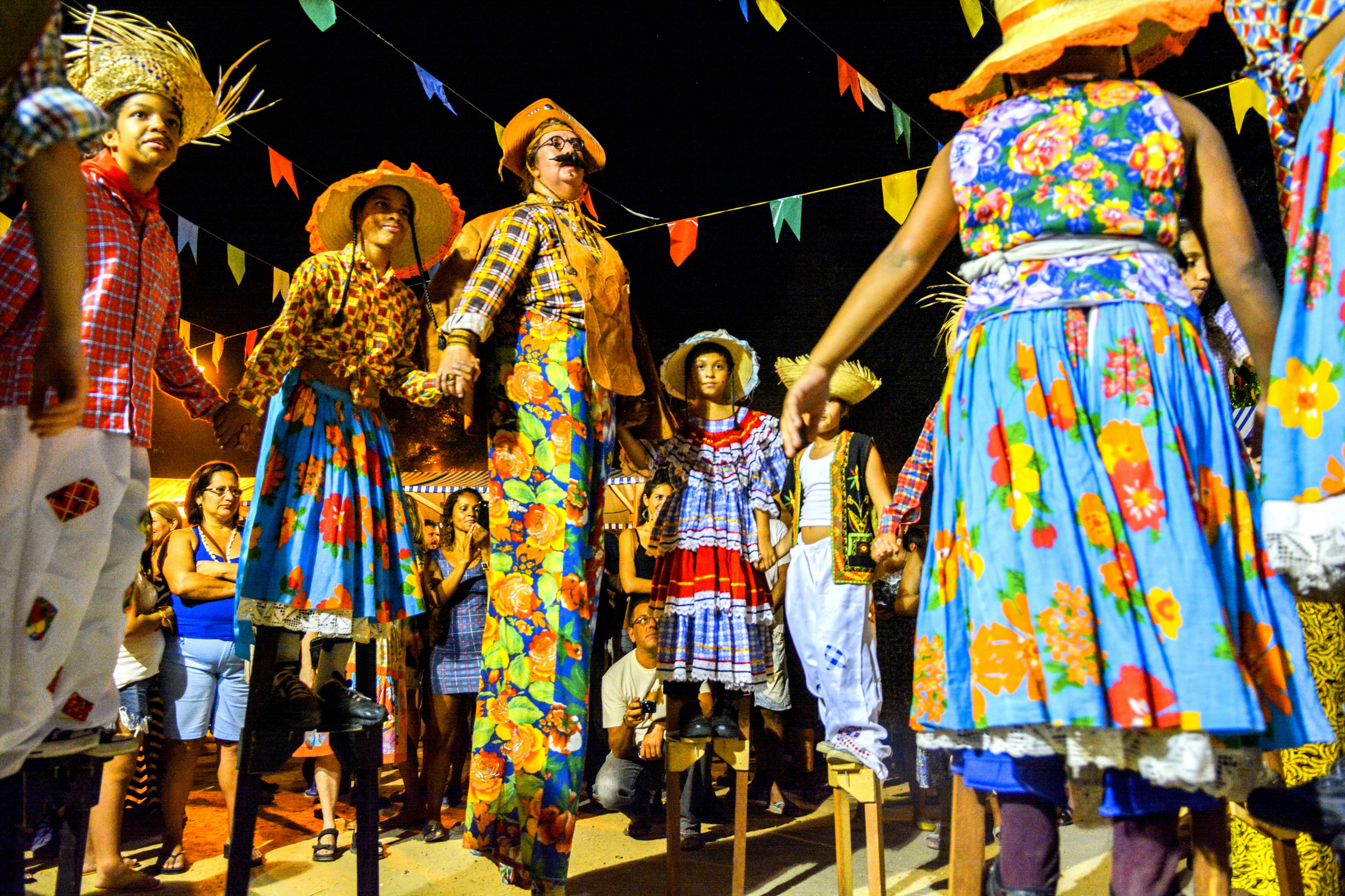People wear costumes with printed fabric and straw hats as they dance in the street during an outdoor celebration.