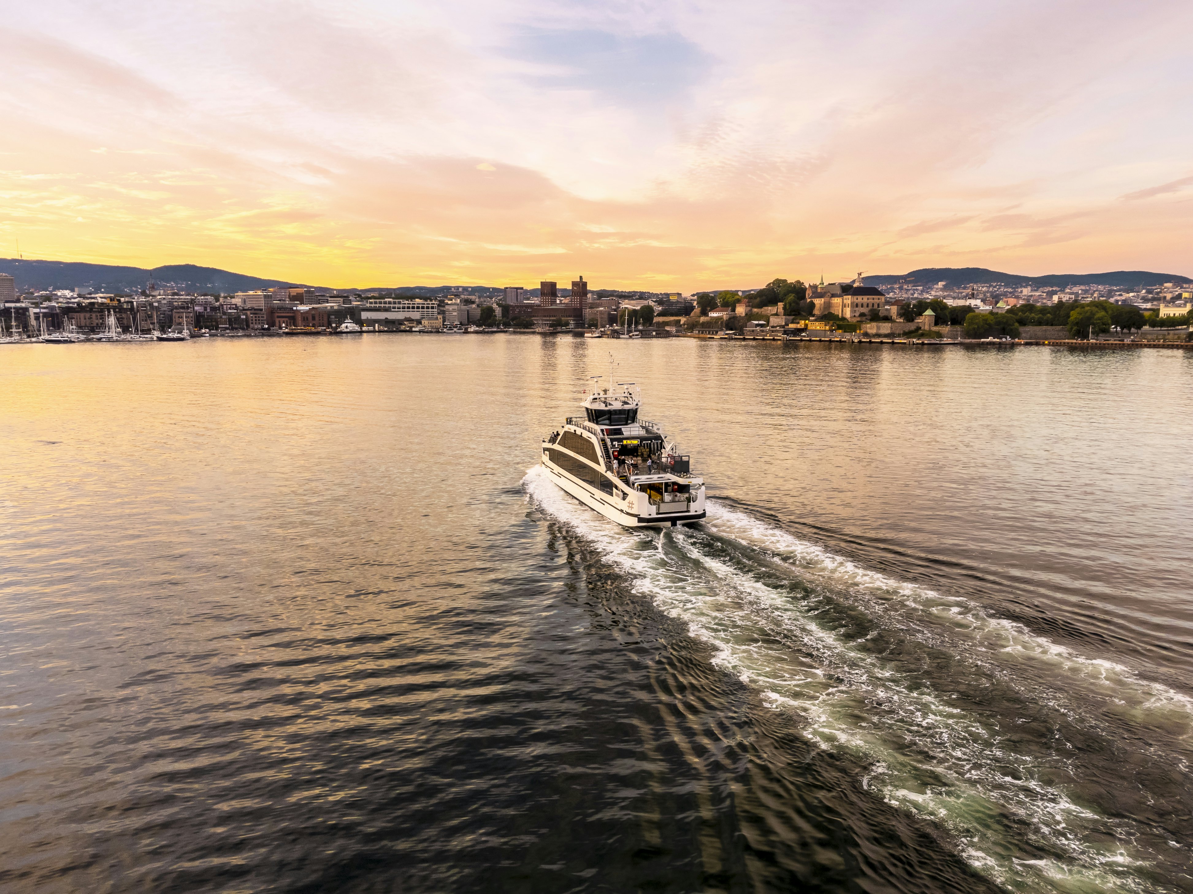 A small passenger boat traveling towards a city harbor as the sun sets.