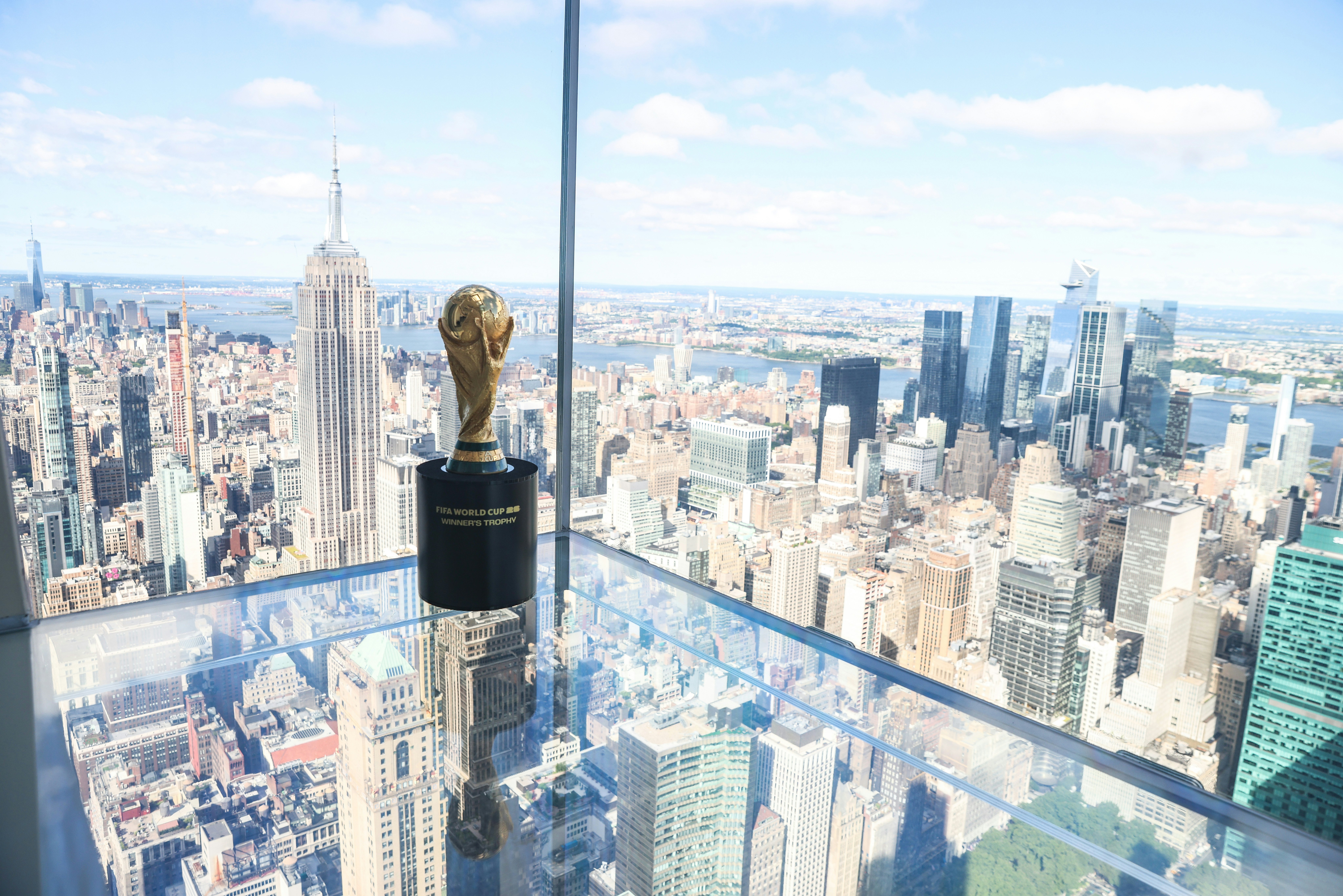 A gold trophy is pictured against the panoramic window of a skyscraper. The dense skyline of a huge city is visible on the other side of the glass.